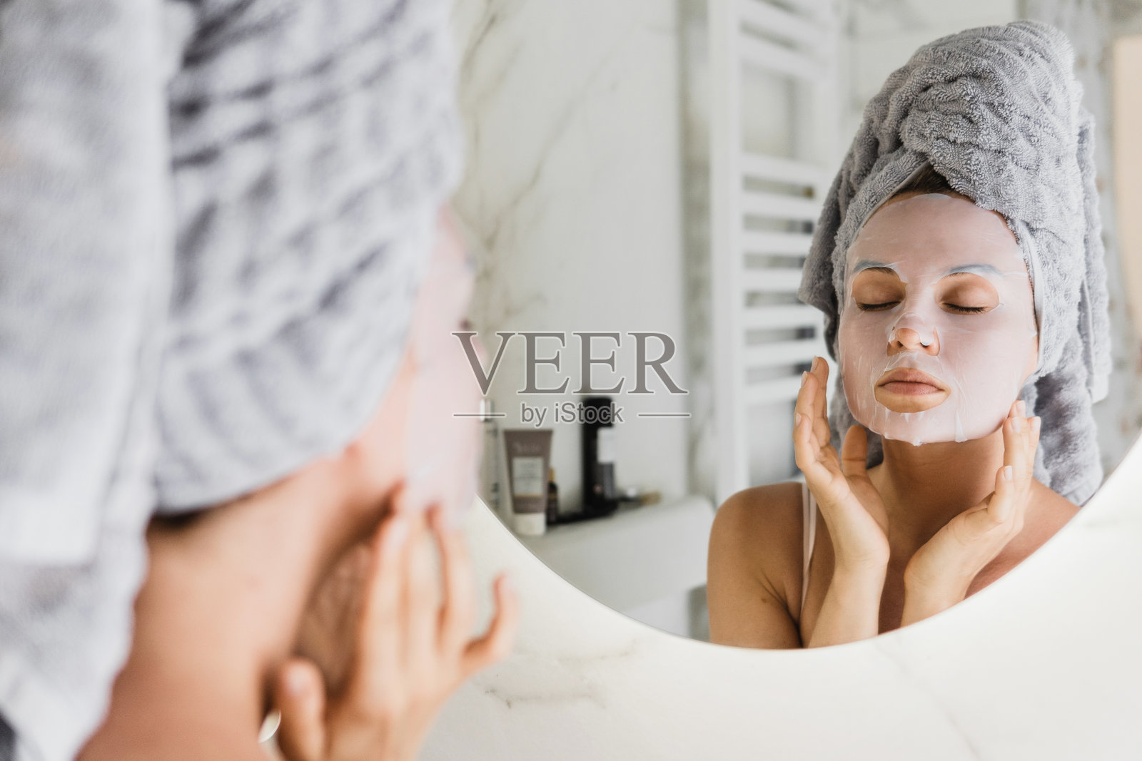 一个女人在浴室里，脸上敷着面膜，看着镜子照片摄影图片
