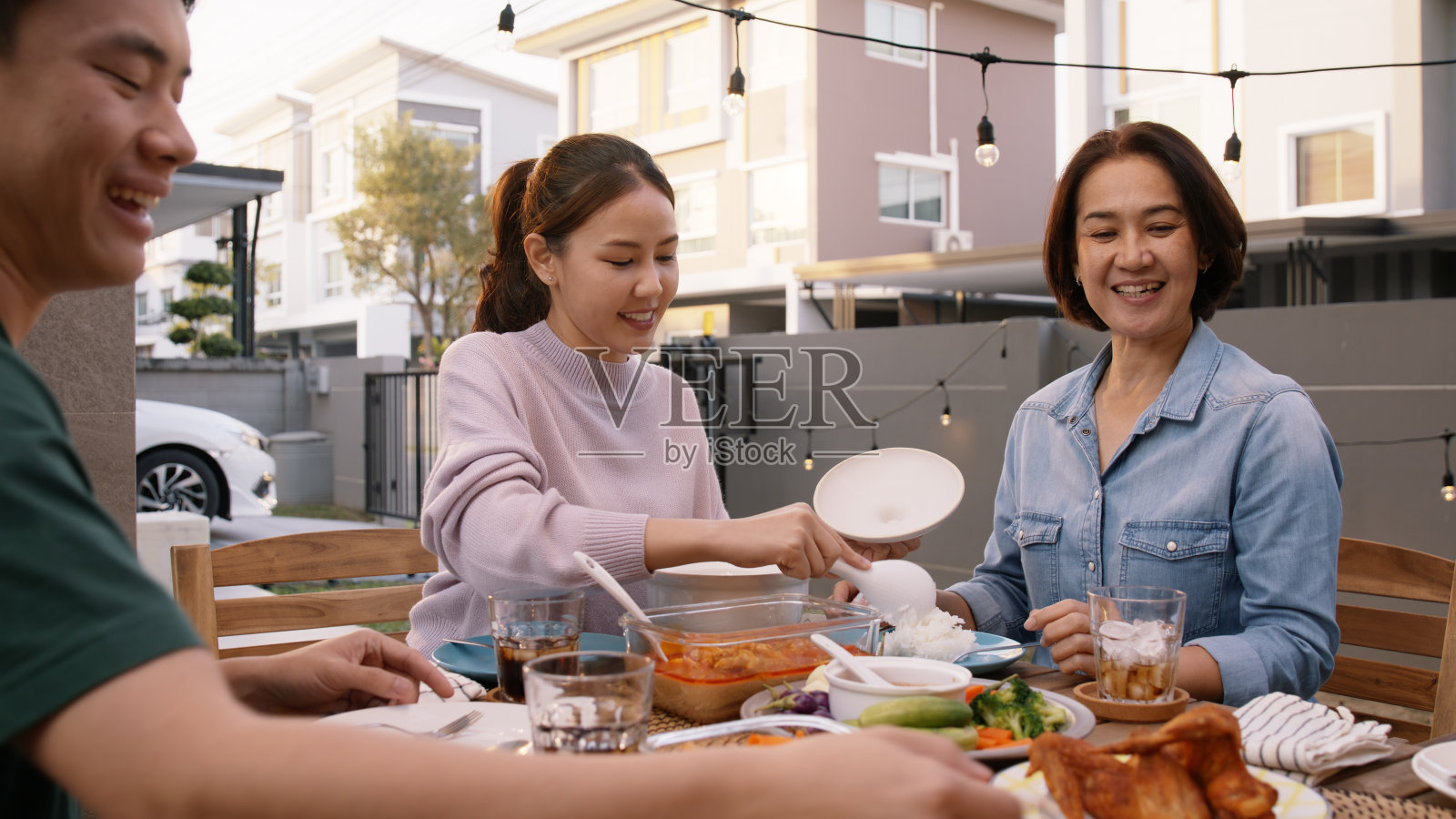 爱心照顾者母亲节分享服务勺饭通行证中年妈妈在家庭院餐桌聚会。一群年轻的亚洲人享受温暖的时间，吃泰国野餐饭给成年父母成熟的妈妈。照片摄影图片