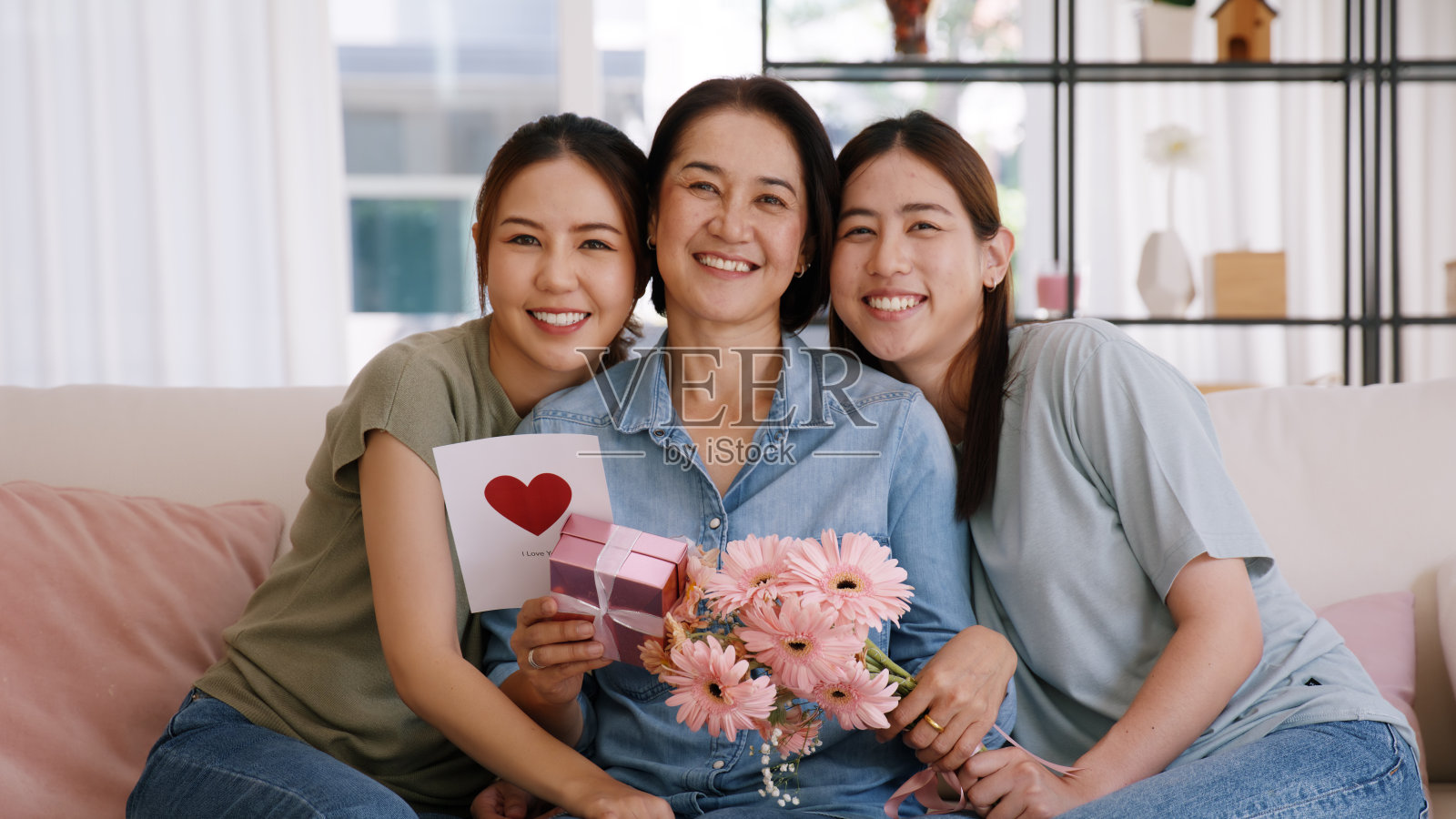 母亲节快乐时光长大的孩子看着镜头拥抱给成熟的妈妈送鲜花礼盒红心卡。爱吻呵护妈妈亚洲中年成年人喜欢坐在家里的沙发上微笑。照片摄影图片