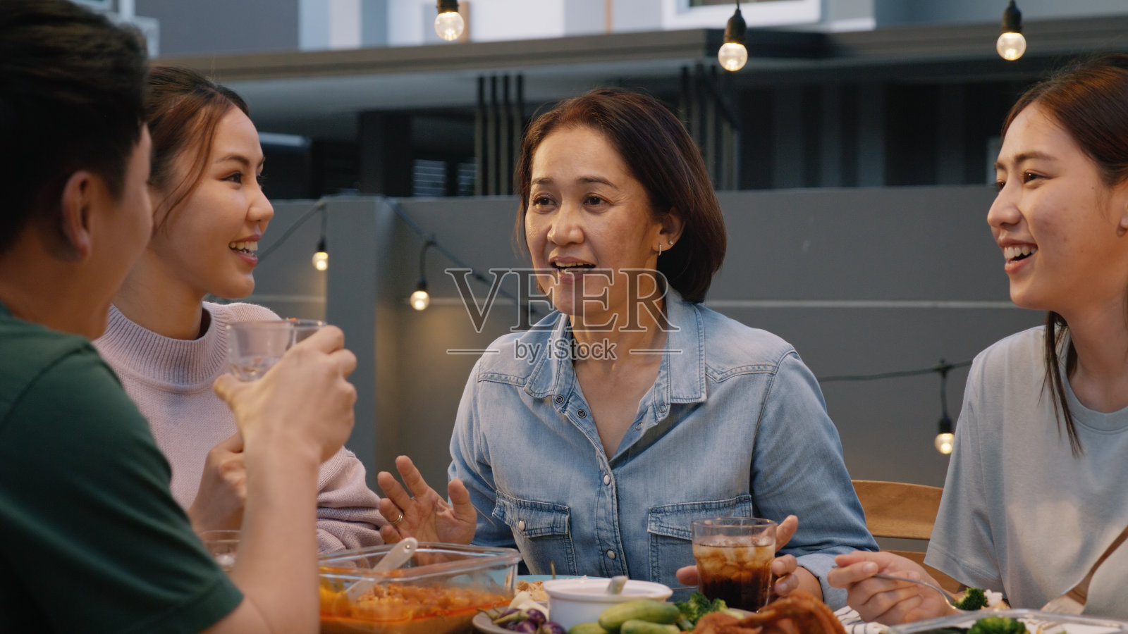 中年妈妈在饭桌上谈笑风生。亚洲人，成年人，老人，妈妈，享受食物，欢乐，欢笑，快乐时光，在舒适的野餐，温暖的时间，晚上，晚餐，周末。年轻的老年妇女放松退休。照片摄影图片