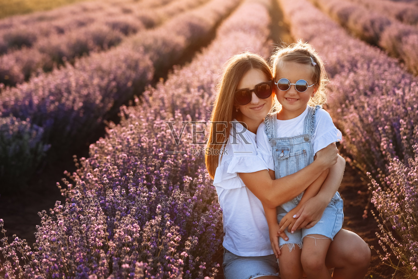 幸福的家庭在紫色的薰衣草田。年轻美丽的母亲和孩子女孩在夏日漫步在盛开的草地上。日落时分，妈妈和美丽的女儿在大自然中玩耍。母亲节照片摄影图片