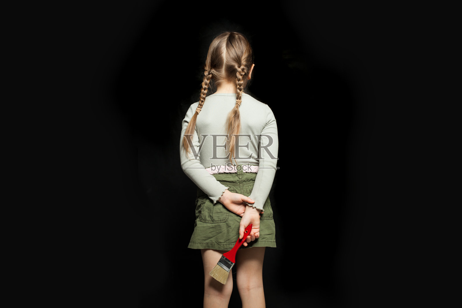 小女孩背对着黑板，拿着画笔站在黑板的背景上照片摄影图片