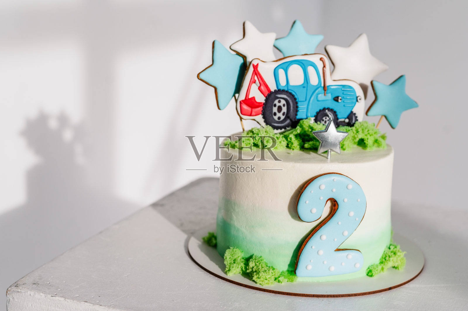 2岁生日蛋糕。蛋糕上有一个图形拖拉机和星星装饰的绿色，蓝色的装饰为男孩。生日聚会上美味的招待会。节日甜品的概念。放文字的地方。照片摄影图片