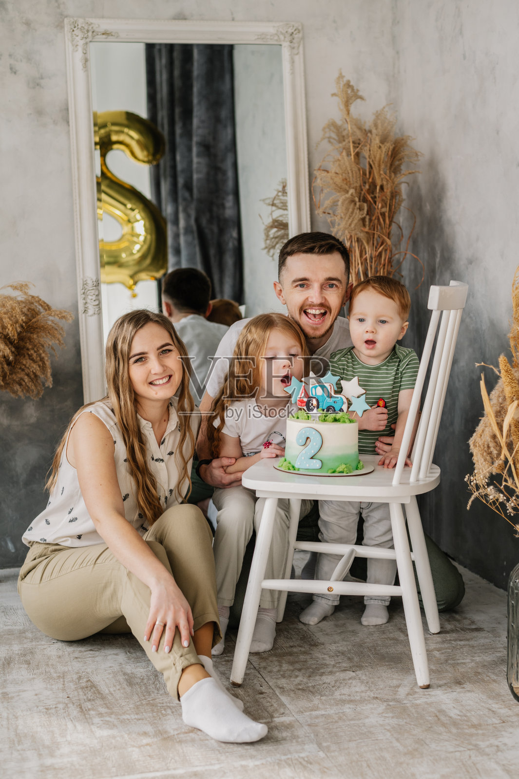 妈妈，爸爸抱着孩子。生日宴会。妈妈、爸爸、女儿在工作室祝贺儿子生日。快乐的家庭在蛋糕上吹蜡烛，开心地庆祝生日派对2年。照片摄影图片