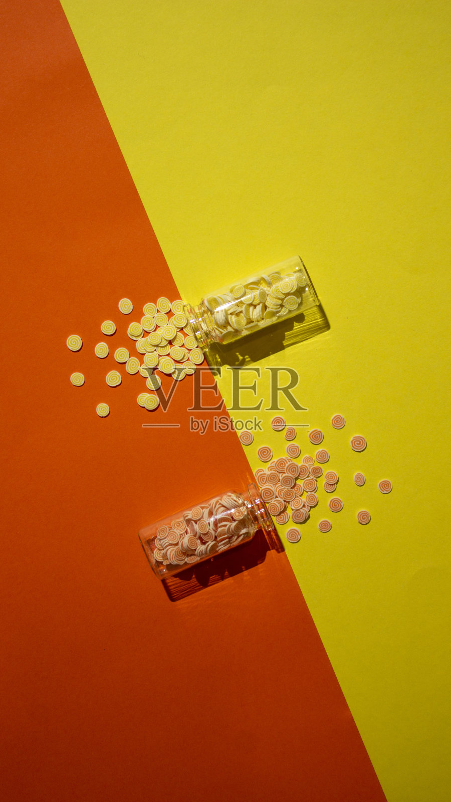 橙色和黄色背景上打翻了小瓶子，洒了糖果。照片摄影图片