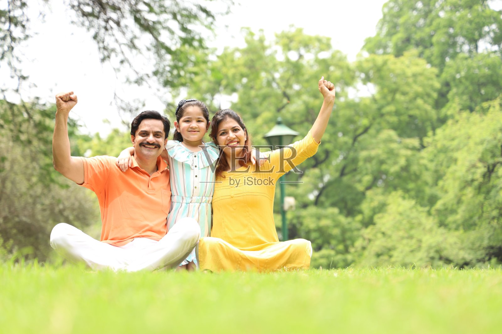 快乐的印度小家庭坐在草地上，享受他们的家庭时光。照片摄影图片