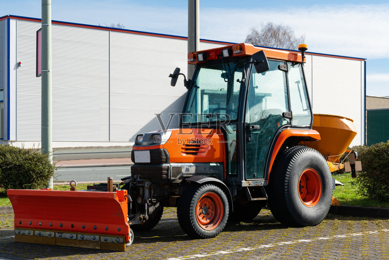 一辆橙色的小型轮式拖拉机停在停车场里。照片摄影图片