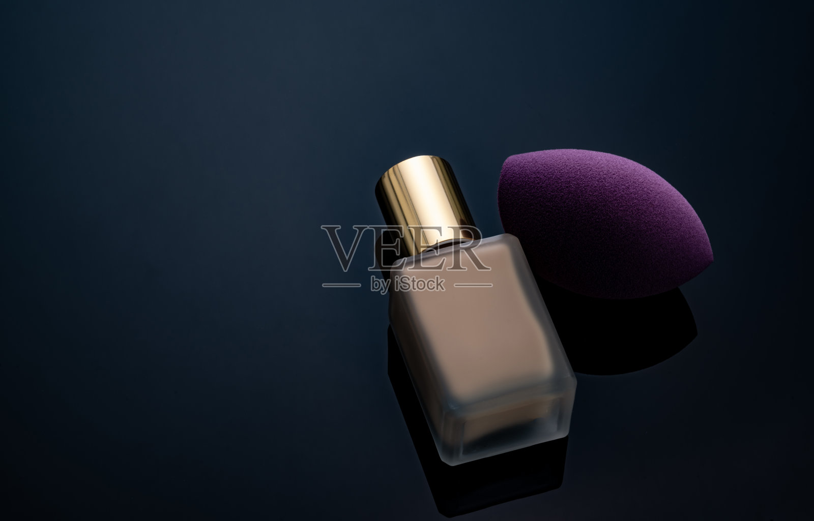 紫色化妆海绵在黑暗的背景。软妆化妆海绵。平端化妆海绵与模糊化妆粉底瓶。液体米色化妆粉底和美容搅拌机。美容产品。照片摄影图片