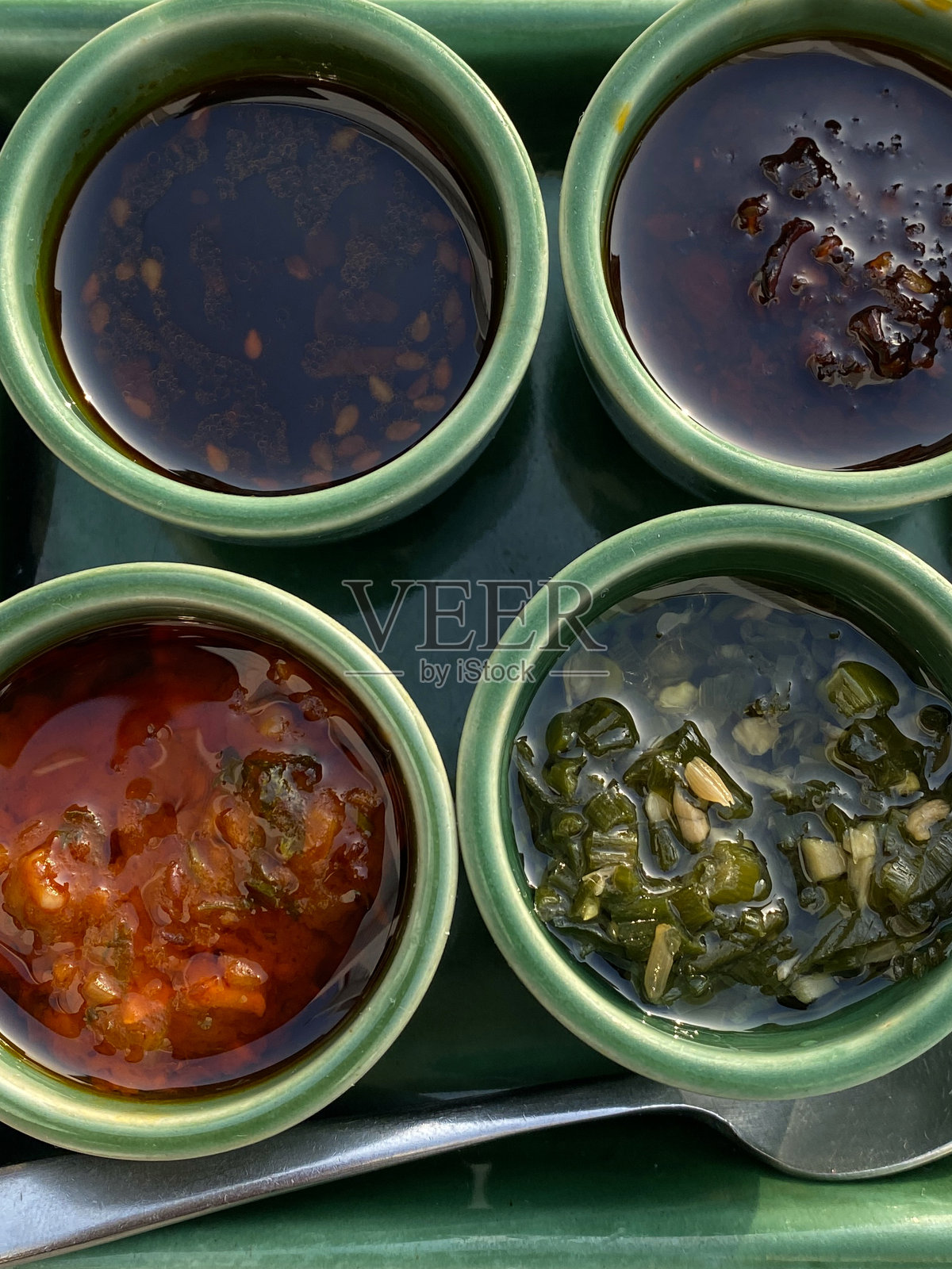 绿色方形盘子的特写图片，有四种蘸酱，用于圆形模子中的饺子，辣椒油，酱油，西红柿和大蒜辛辣调味品，高架俯视照片摄影图片