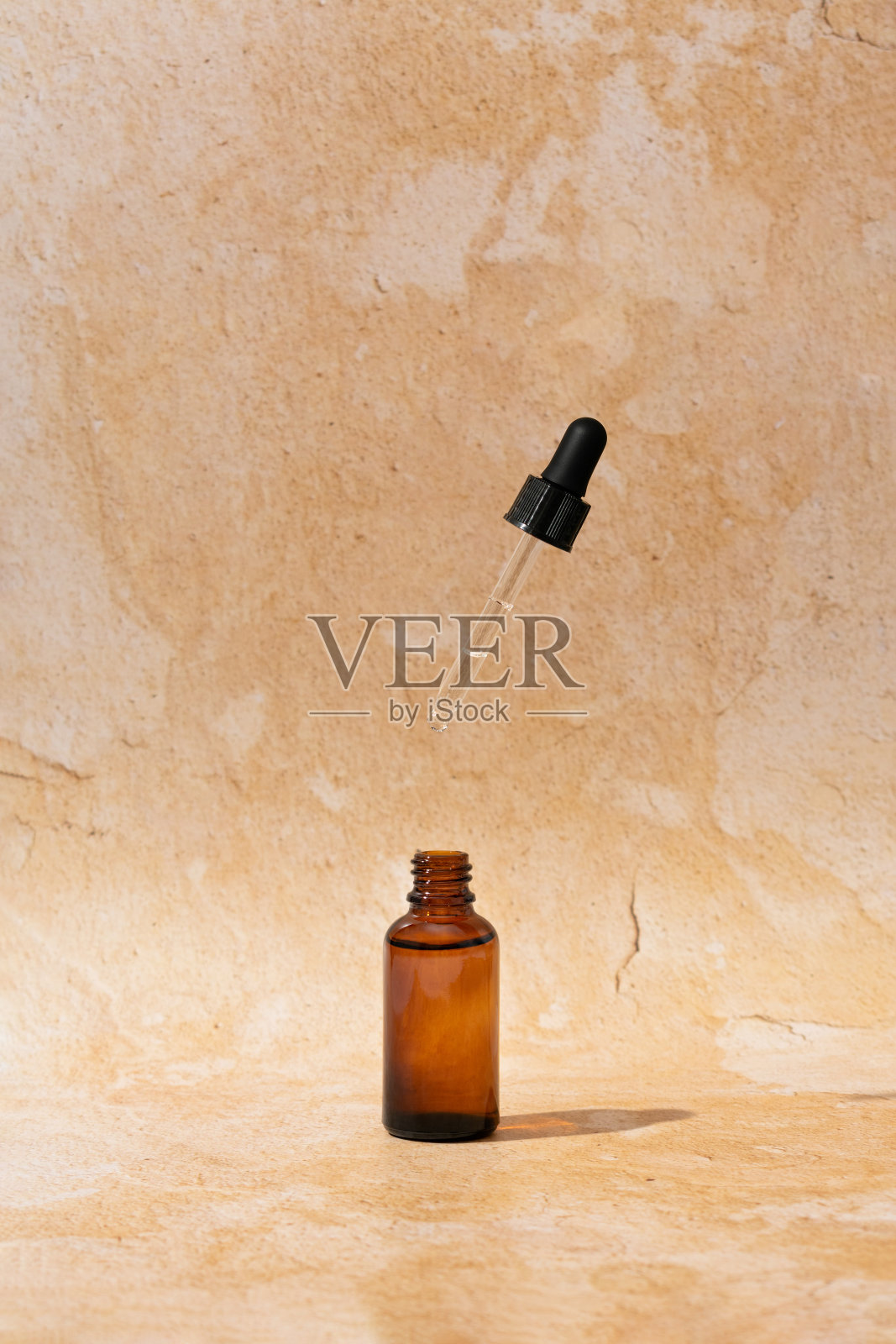 打开棕色玻璃化妆品瓶的面部精华液或精油与滴管在空气中对天然土石背景。极简复古的护肤品成分。照片摄影图片