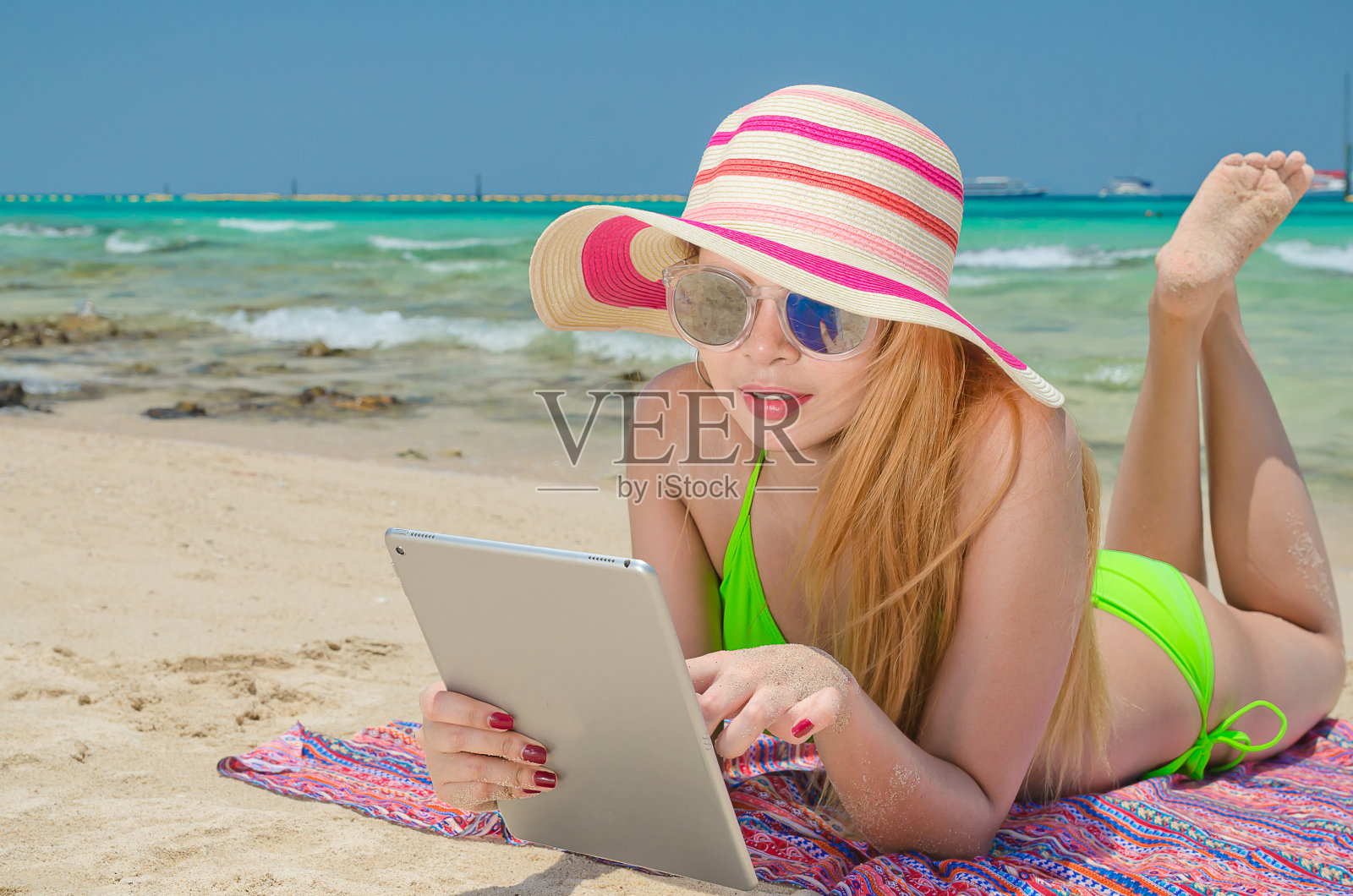 美丽的女人穿着比基尼和帽子睡在沙滩上使用平板电脑照片摄影图片