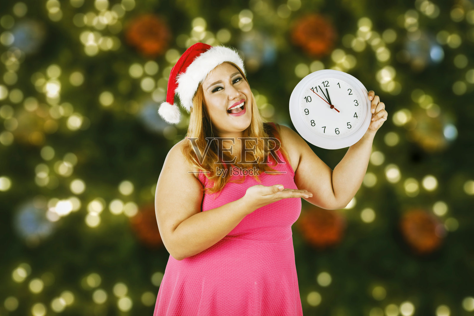 肥胖的女人戴着圣诞老人的帽子，手里拿着一个钟照片摄影图片