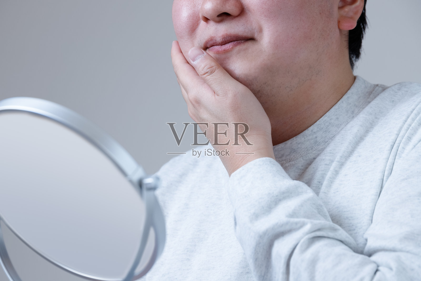 一位亚洲男子微笑着抚摸着自己的皮肤，他感受到了护肤和剃须后的效果。照片摄影图片