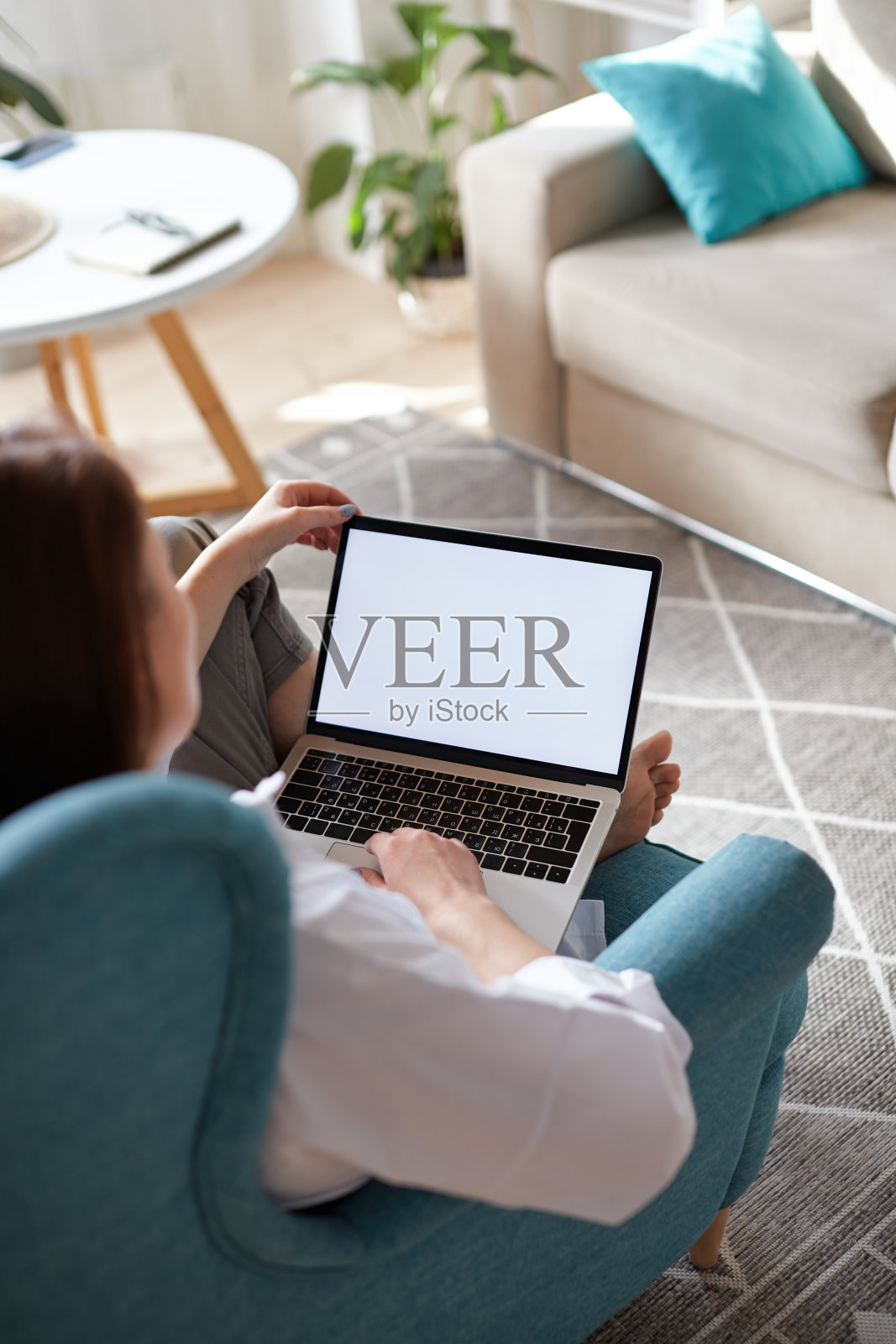 模拟白屏笔记本电脑的女人坐在家里的扶手椅上使用电脑，背对着屏幕照片摄影图片