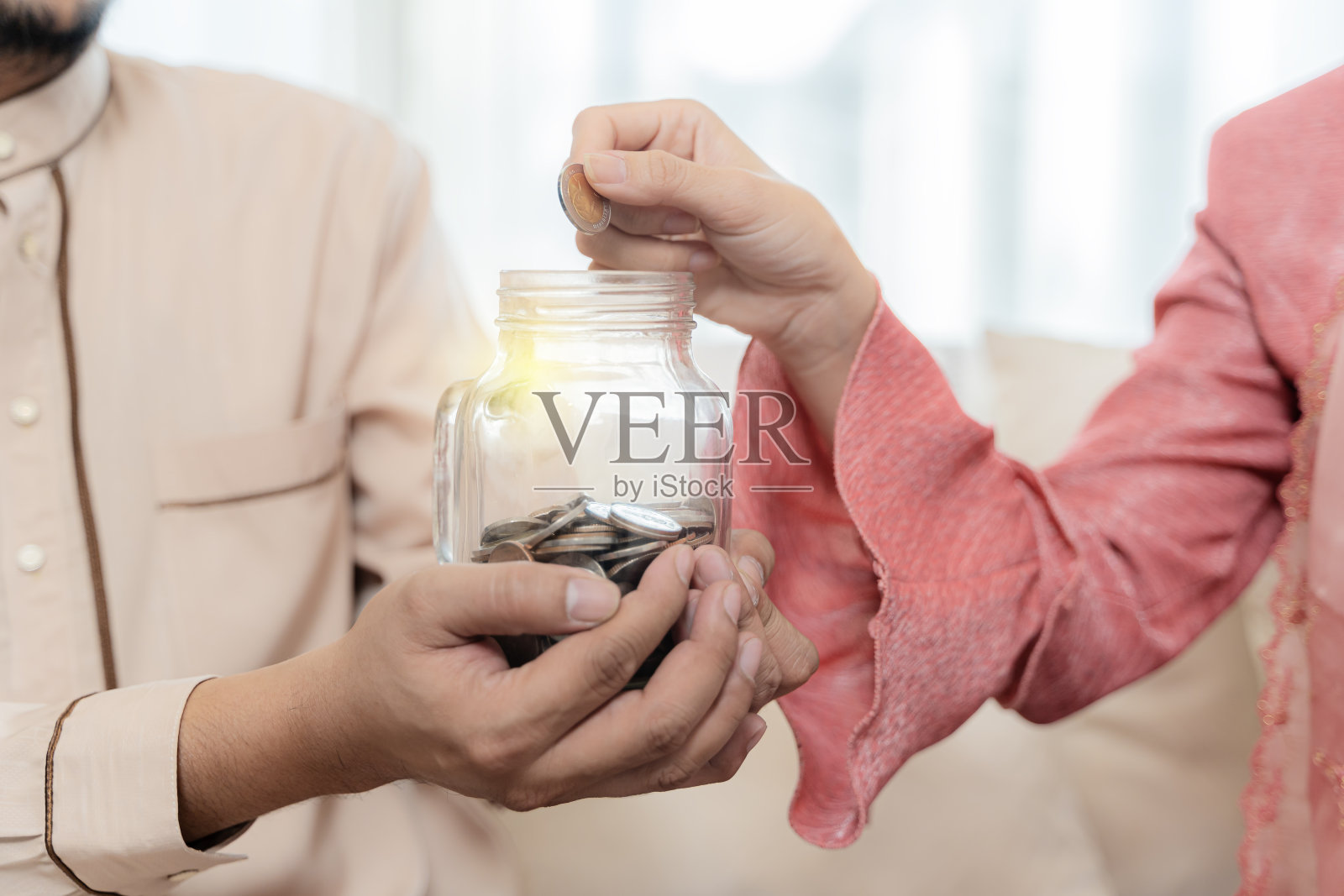 女人把钱放在男人手里标有的玻璃罐里，储蓄和投资钱，为将来做准备——储蓄理财理念照片摄影图片