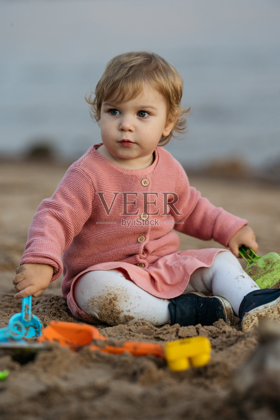 白人幼女在沙滩上玩玩具的照片。照片摄影图片