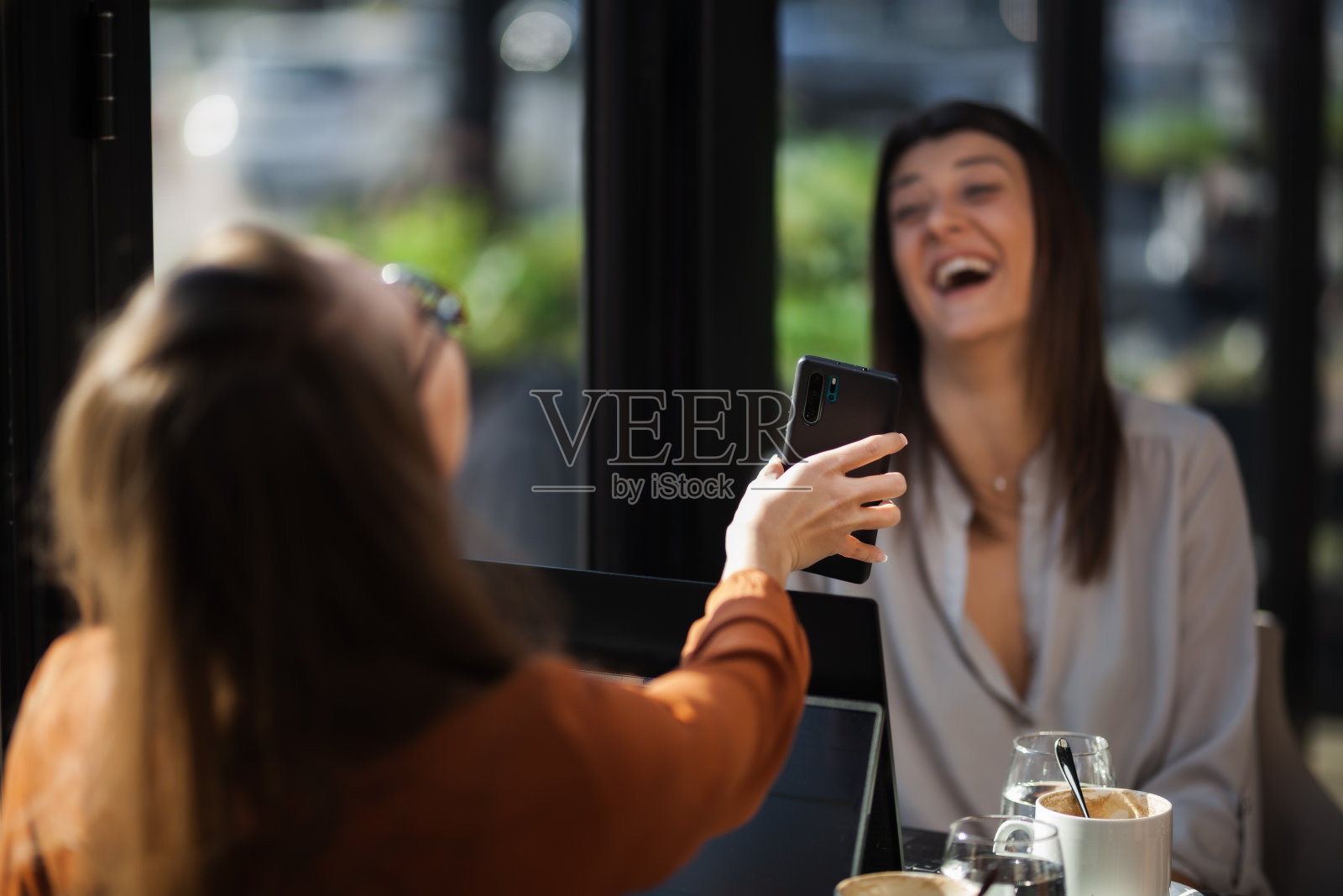 两个年轻的女商人在咖啡馆里进行一对一的会谈。下班后，朋友们在靠窗的桌子旁聊着八卦，喝着咖啡，思考着……照片摄影图片