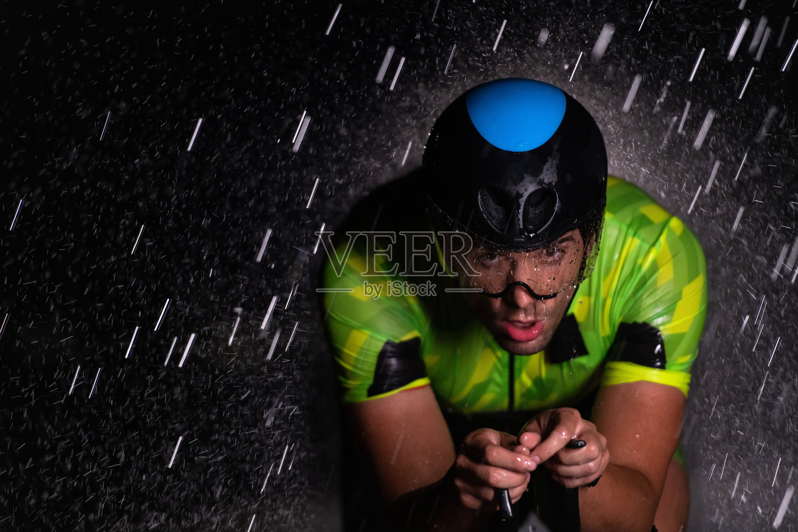 一名铁人三项运动员冒着雨骑着自行车穿过黑夜，为即将到来的马拉松做准备。前景中模糊的雨滴和背景中黑暗、忧郁的气氛增加了at所表现出的决心和坚毅感照片摄影图片