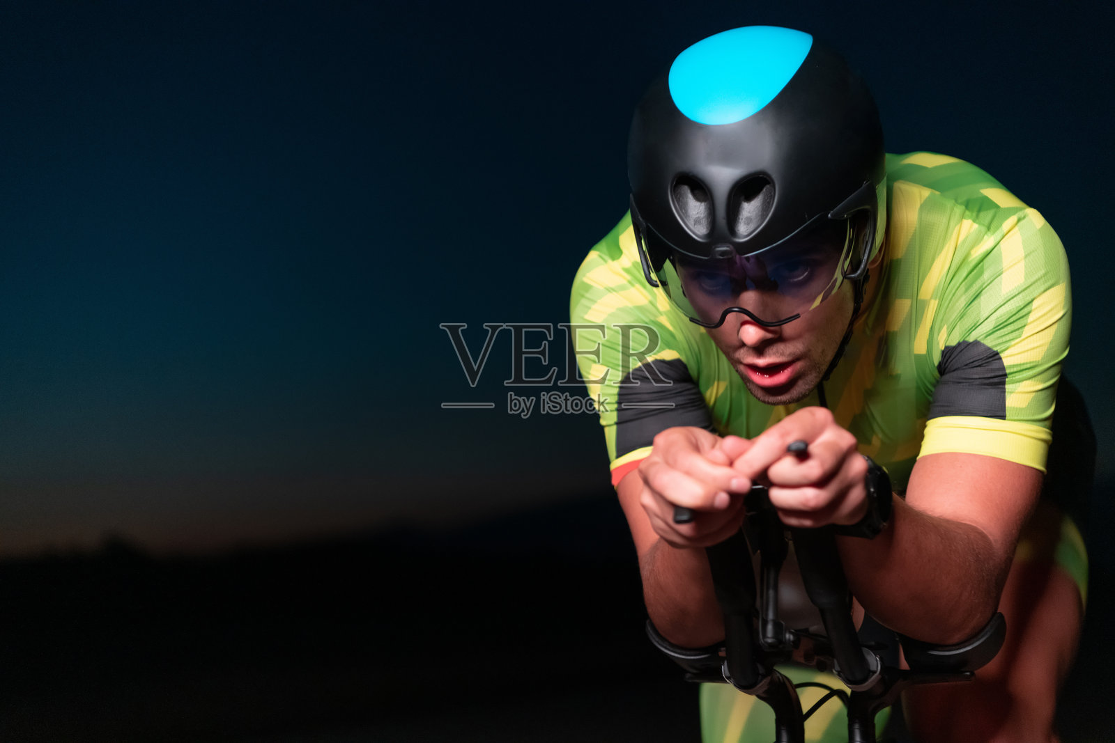 一个铁人三项运动员在漆黑的夜晚骑着自行车，强迫自己为马拉松做准备。自行车上的光线与黑暗的对比营造出一种戏剧性，突出了运动员的决心和毅力。照片摄影图片