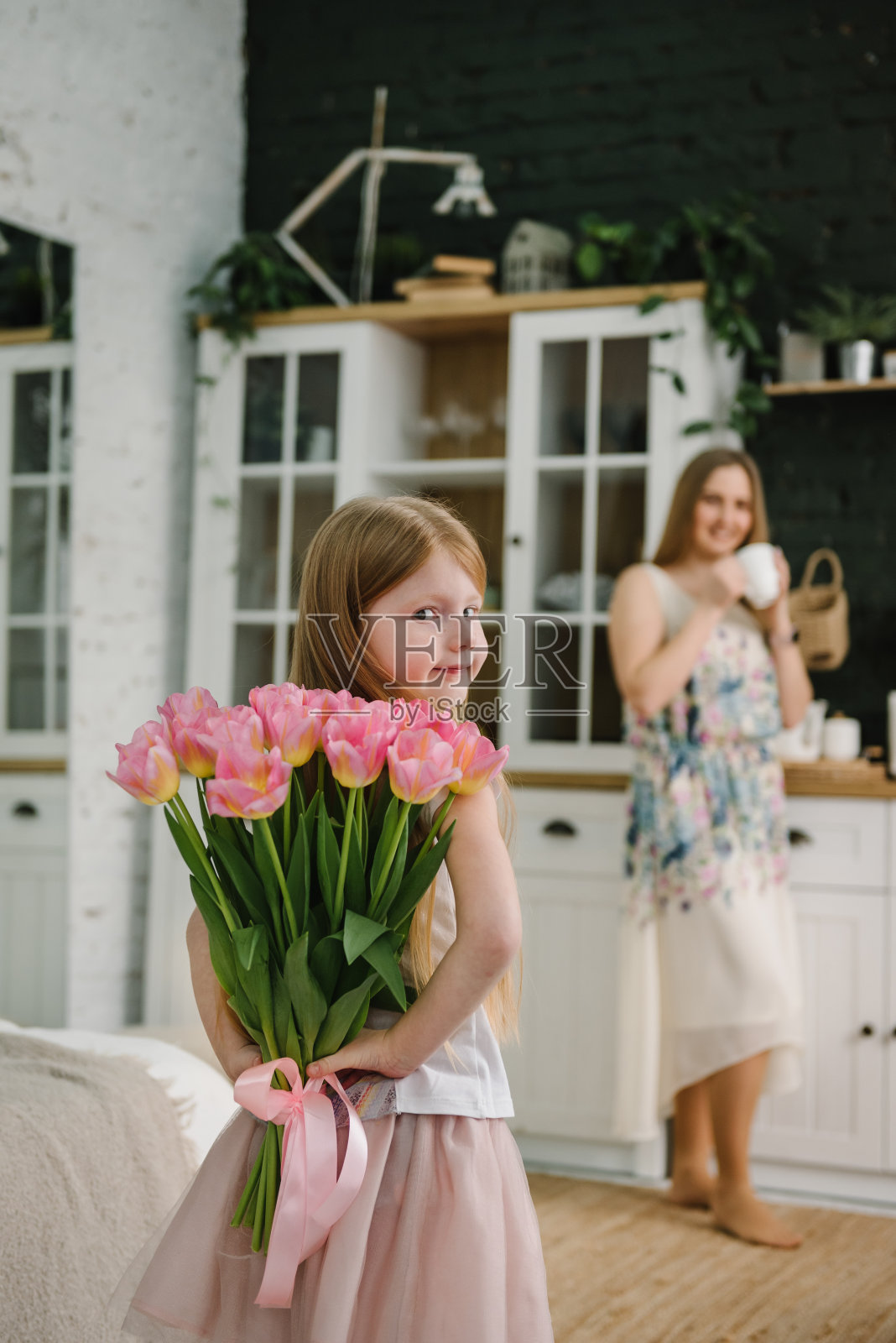 女儿在家里的厨房里向母亲表示祝贺，并送上一束郁金香。母亲节的概念。妈妈和小女孩惊讶地笑着。贺卡。国际妇女节。后视图照片摄影图片