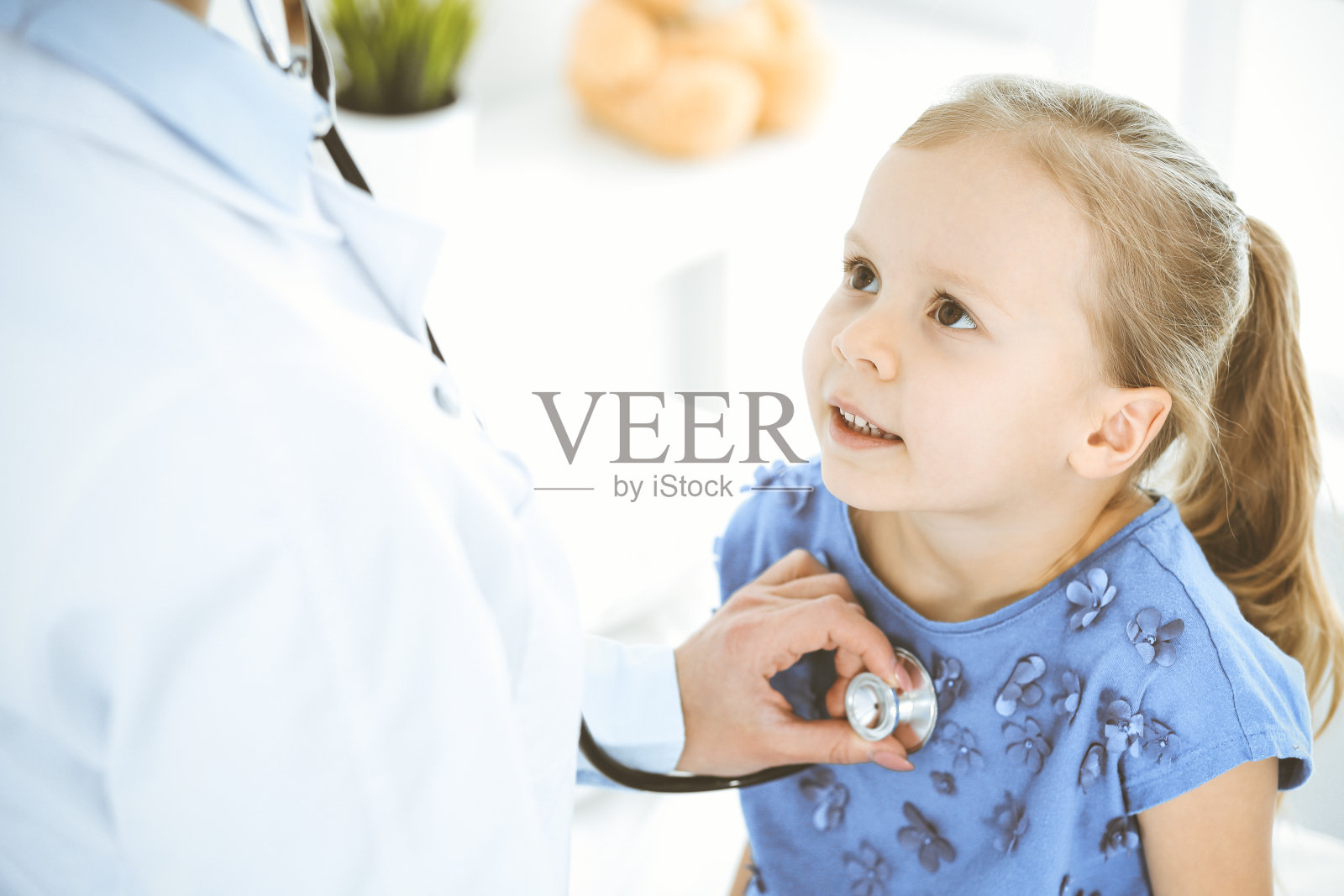 医生用听诊器检查一个小女孩。在例行体检中开心微笑的孩子。医学和保健概念照片摄影图片