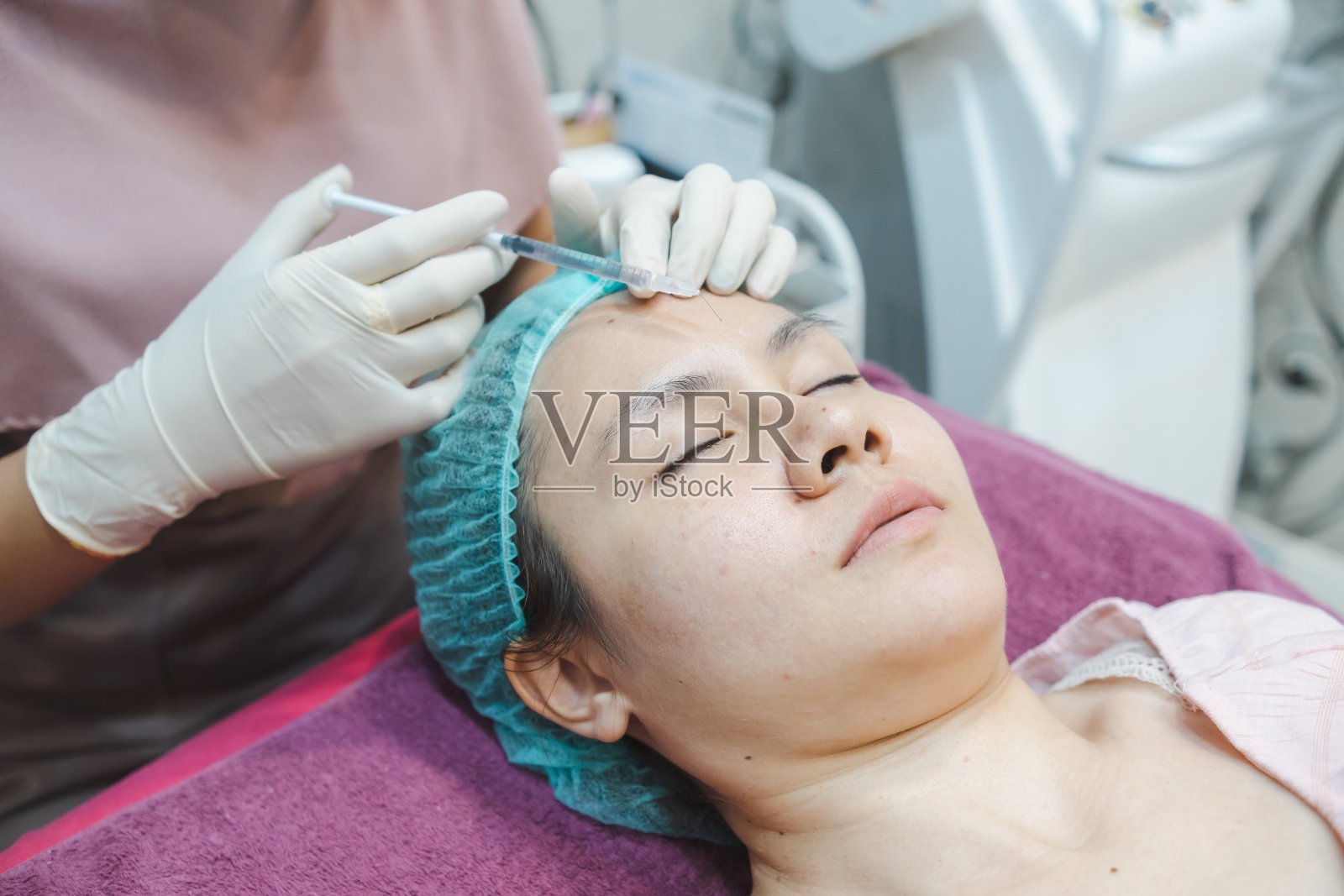 一名护士给一名亚洲妇女的脸上注射皮肤精华液。在美容诊所，医疗和美容皮肤科预约概念。照片摄影图片