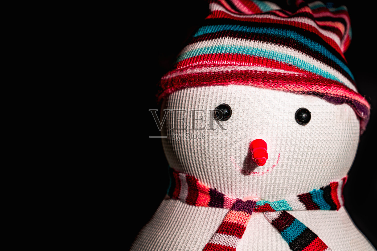 一个雪人在黑色背景上戴着条纹帽子和围巾照片摄影图片