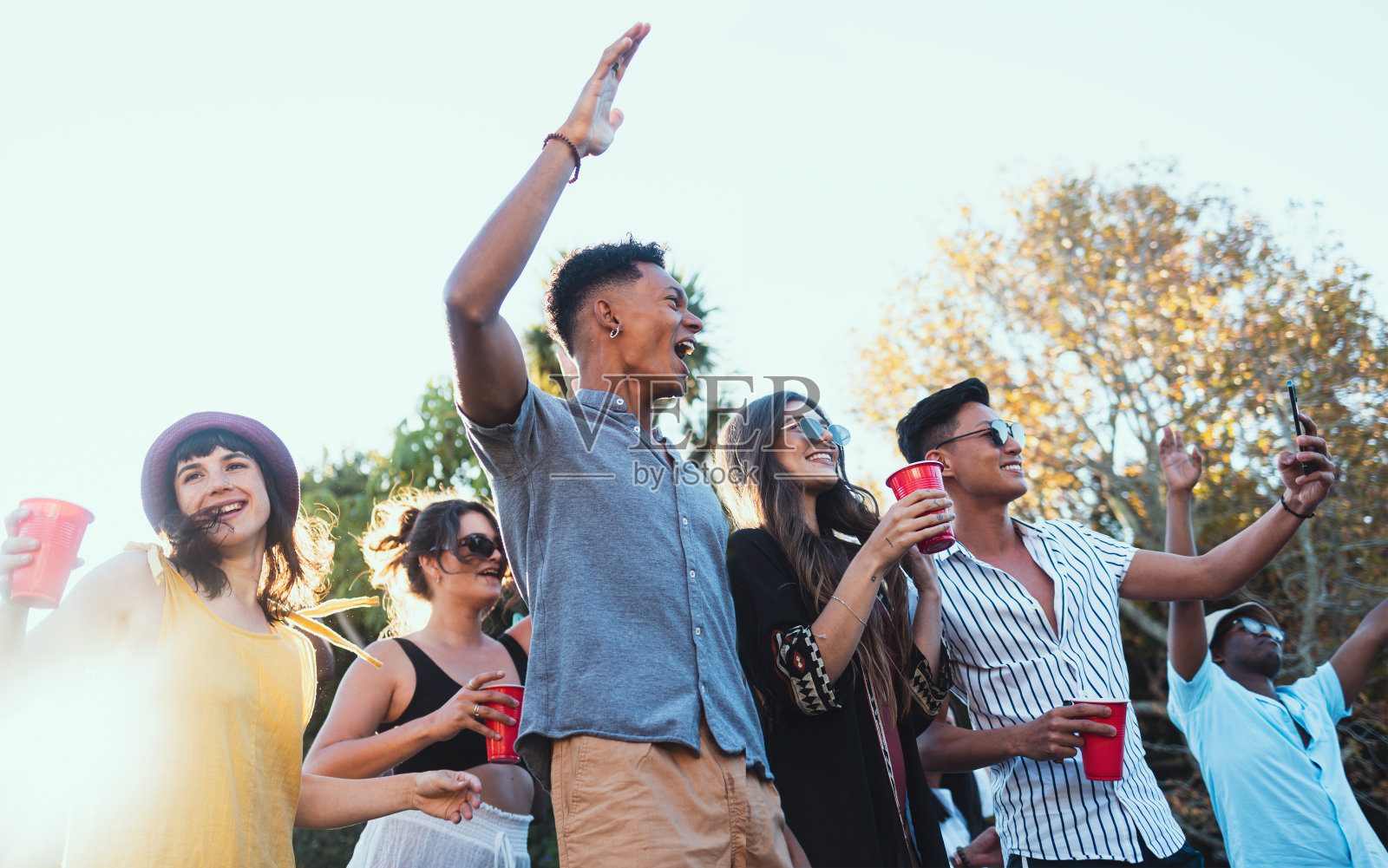 在节日、音乐会或夏季社交活动中，与一群朋友一起在户外喝酒、聚会和庆祝。形形色色的青年男女们在一起一边跳舞，一边兴高采烈地喝着酒照片摄影图片