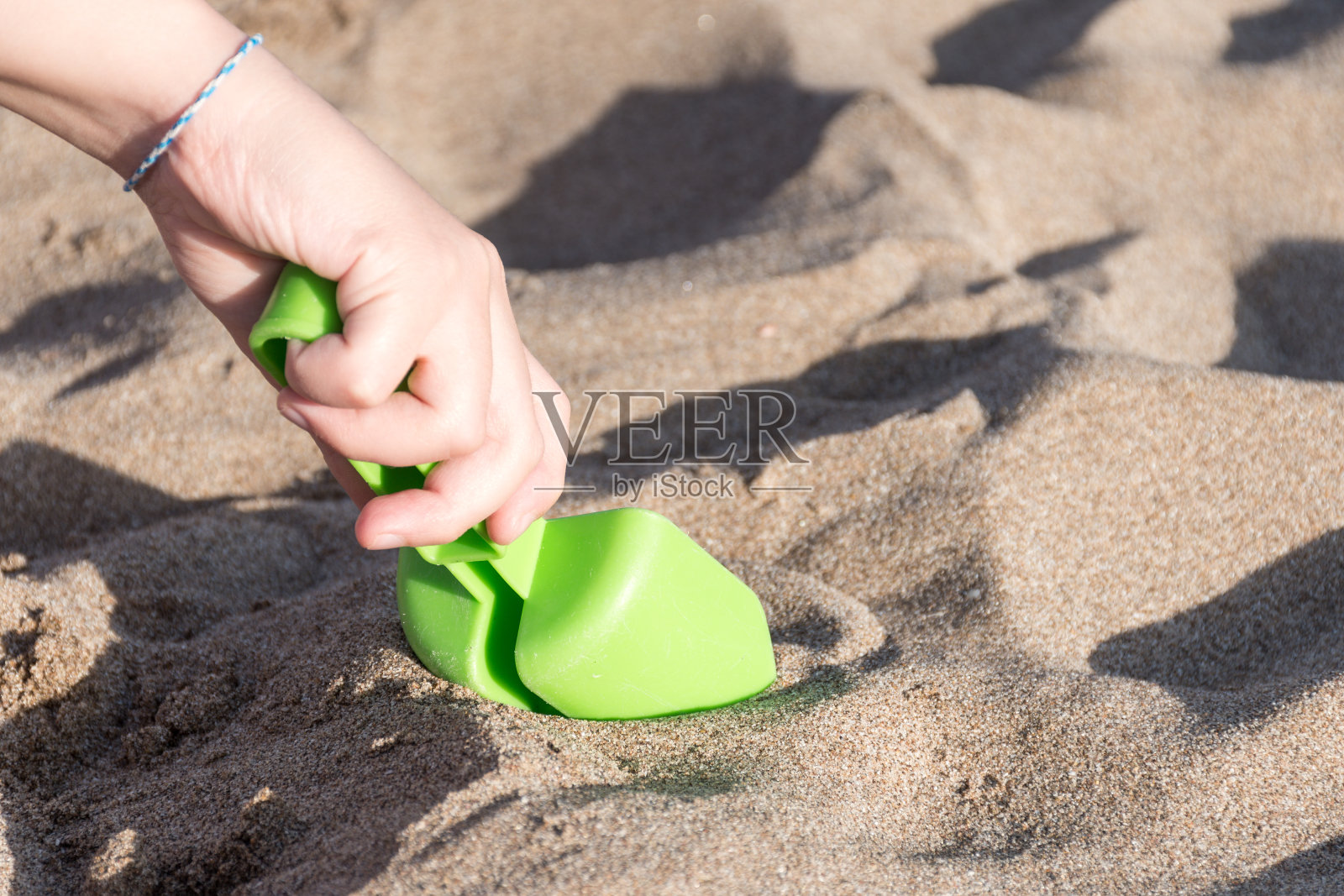 孩子的手在沙滩上玩一根绿色的棍子。照片摄影图片