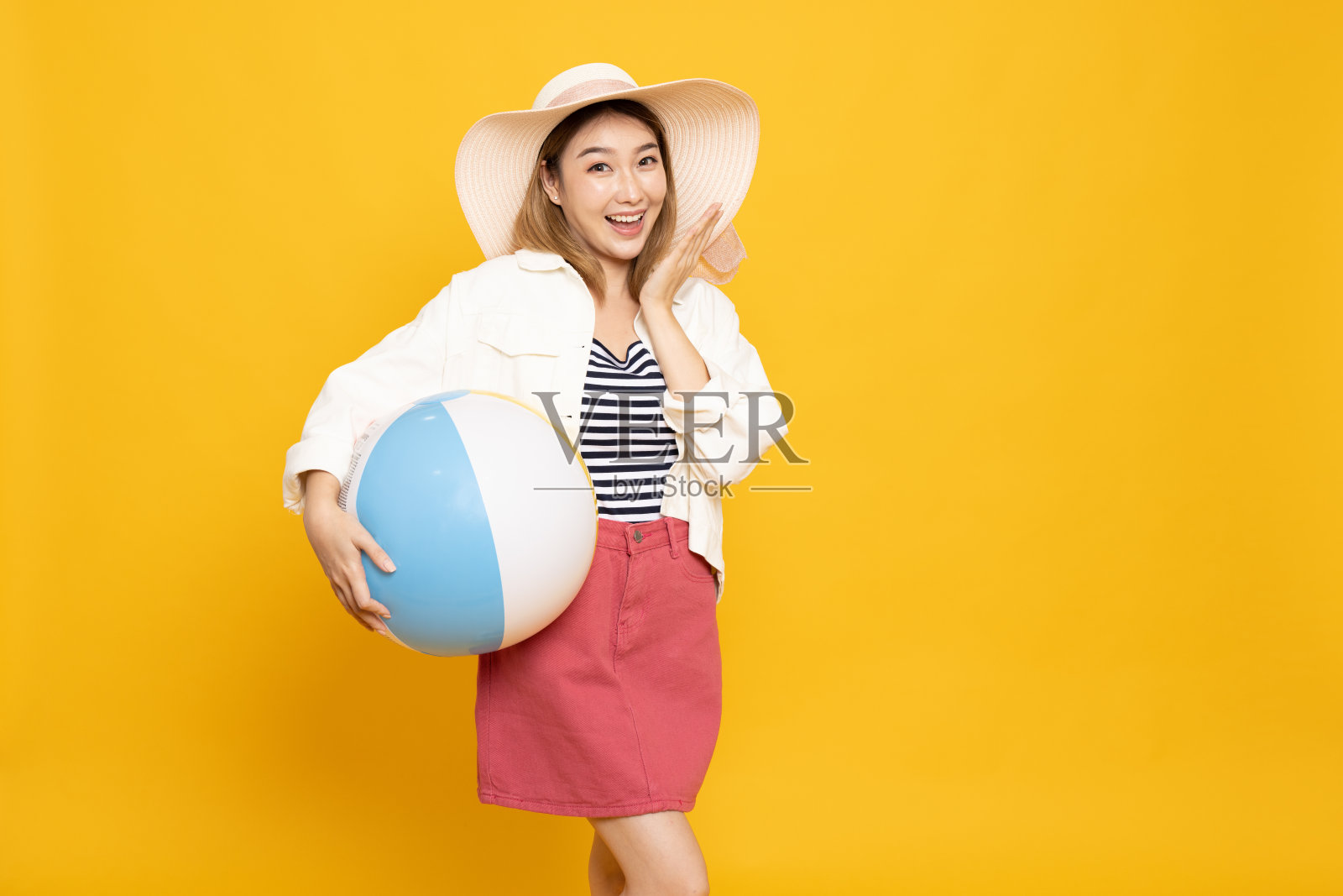 快乐美丽的年轻亚洲女子拿着沙滩球，戴着遮阳帽孤立的黄色背景，假日概念照片摄影图片
