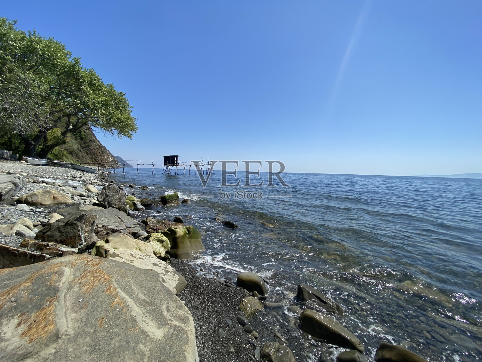 在阳光明媚的夏日，蔚蓝的天空，在渔村的岩石海岸的diy码头上，废弃的木制高跷塔屋渔民洞穴照片摄影图片