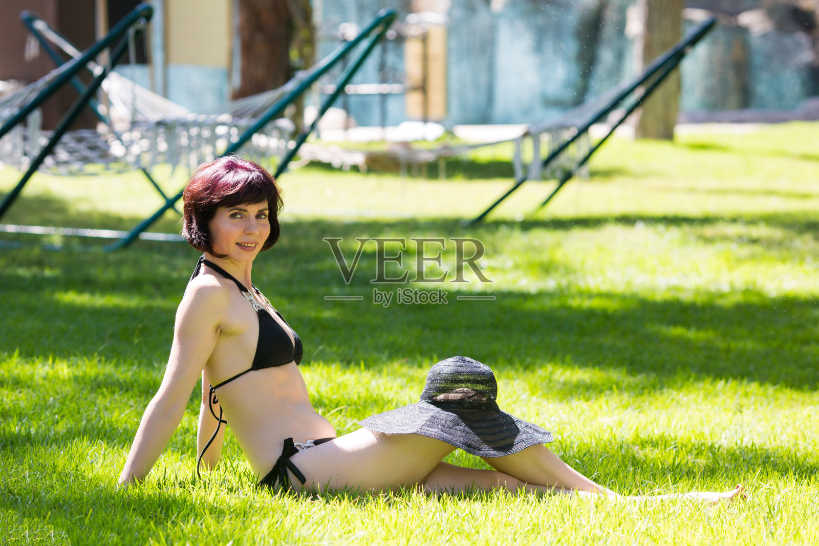 身穿黑色比基尼的黑发美女坐在草地上晒日光浴照片摄影图片