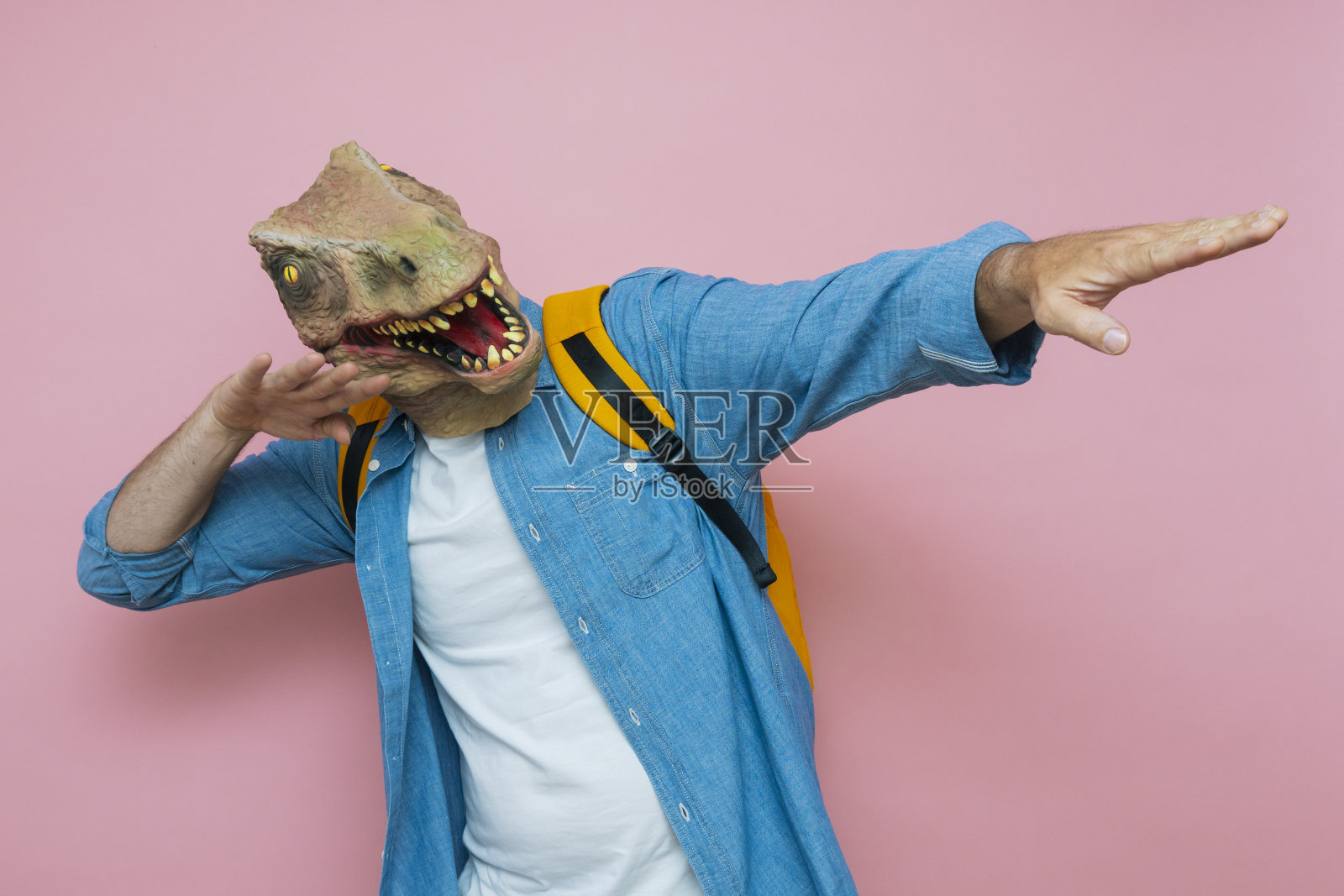 背着双肩包，带着粉红色背景的蜥蜴面具的男人。照片摄影图片