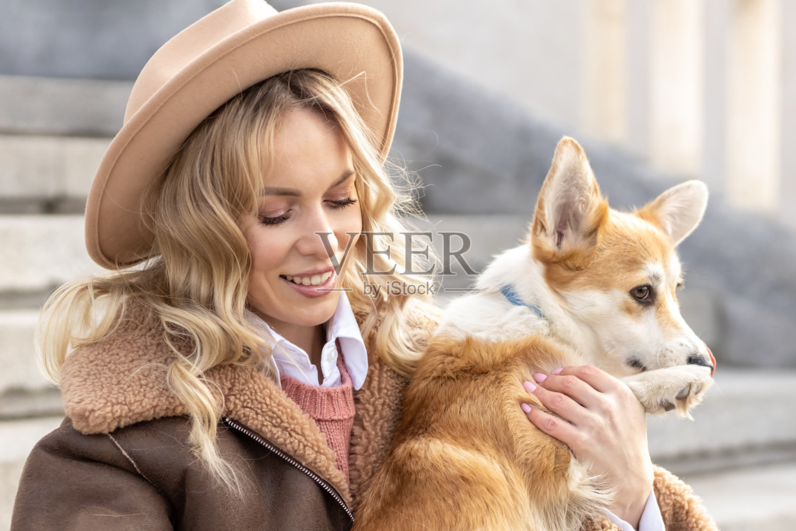 一位戴着帽子的年轻金发女子和威尔士柯基彭布罗克犬在公园散步。春天照片摄影图片