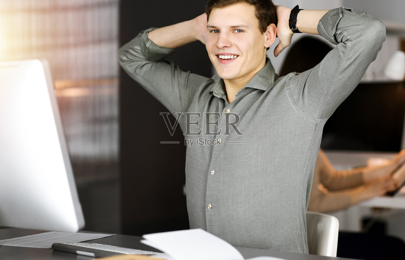 在阳光明媚的办公室里，一头棕色卷发、身穿绿色衬衫的年轻商人在电脑前辛苦工作后伸出双手照片摄影图片