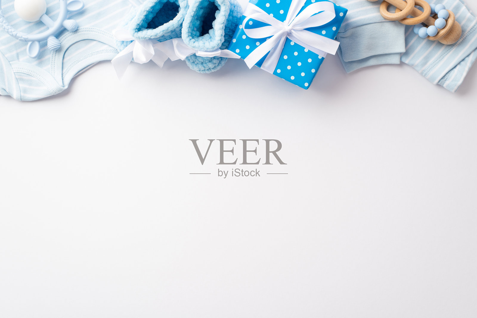 婴儿派对的概念。蓝色婴儿衣服的顶视图照片衬衫裤子针织靴礼盒与丝带蝴蝶结木制摇铃和牙齿在孤立的白色背景与copyspace照片摄影图片