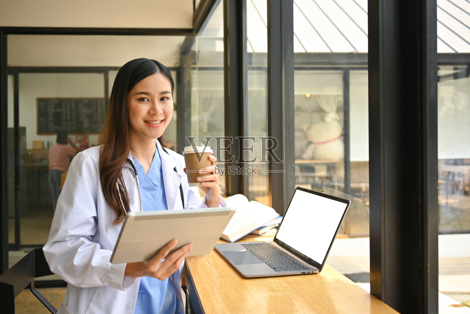 正穿白大褂的女医生在医院食堂休息、喝咖啡、玩数码平板电脑。照片摄影图片