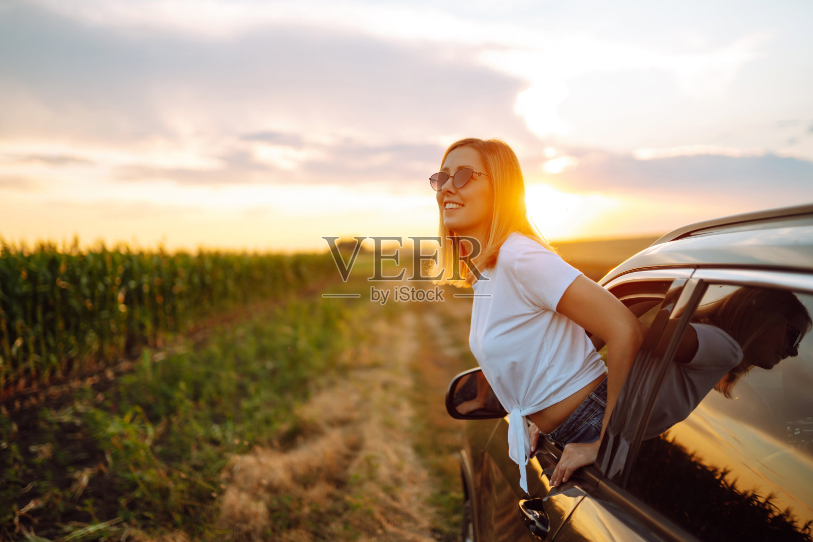 一个快乐的女人从车窗欣赏夕阳。照片摄影图片