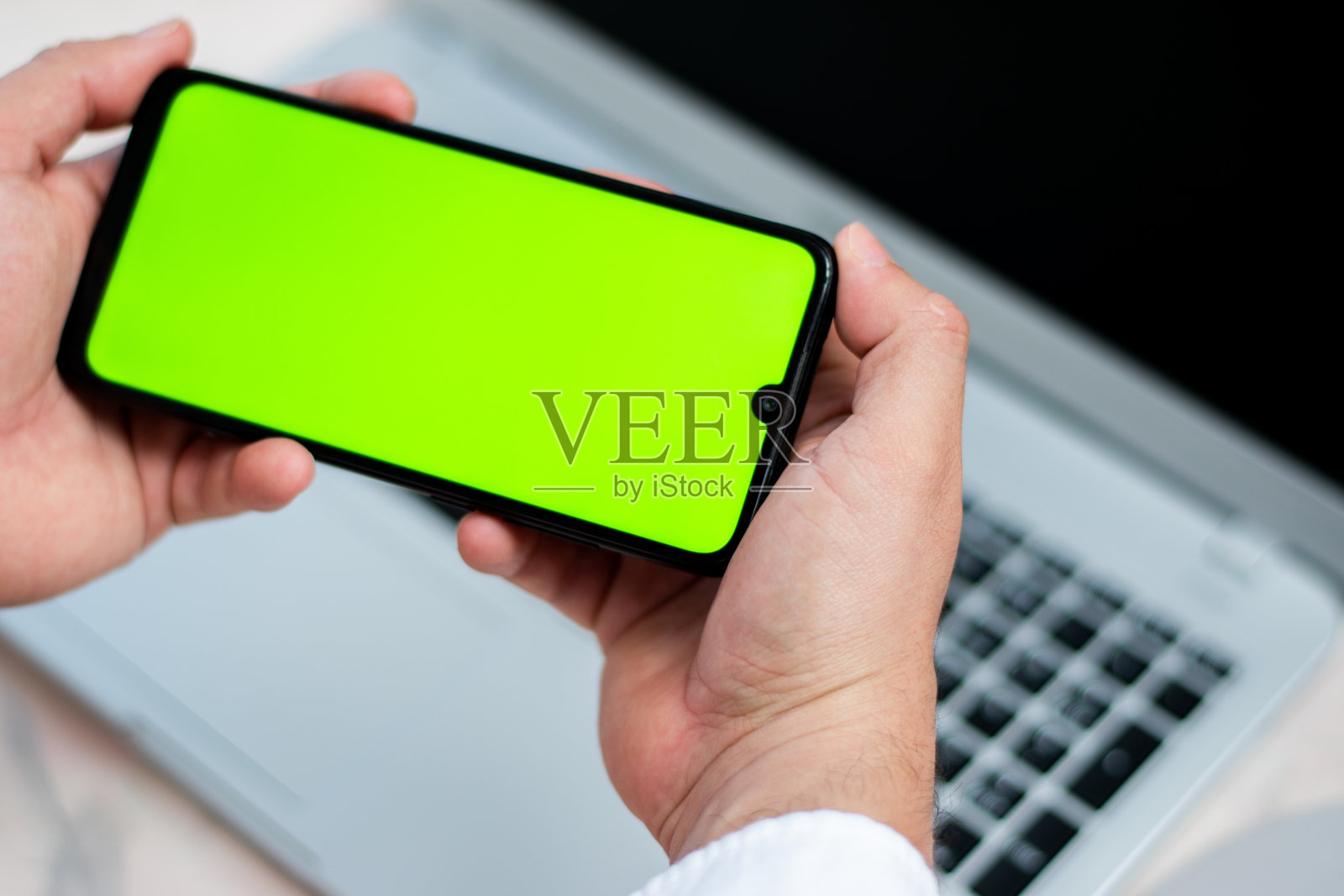 鸟瞰图，一个人水平拿着带色度键的手机在笔记本电脑上照片摄影图片