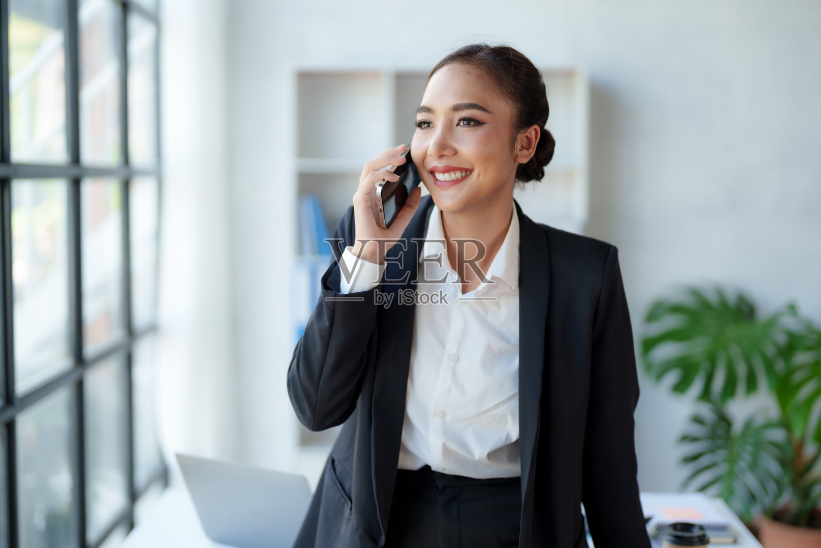 美丽的亚洲商务女性在电话上与客户聊天，在她的笔记本电脑上工作，并在办公室热情愉快地做笔记。照片摄影图片