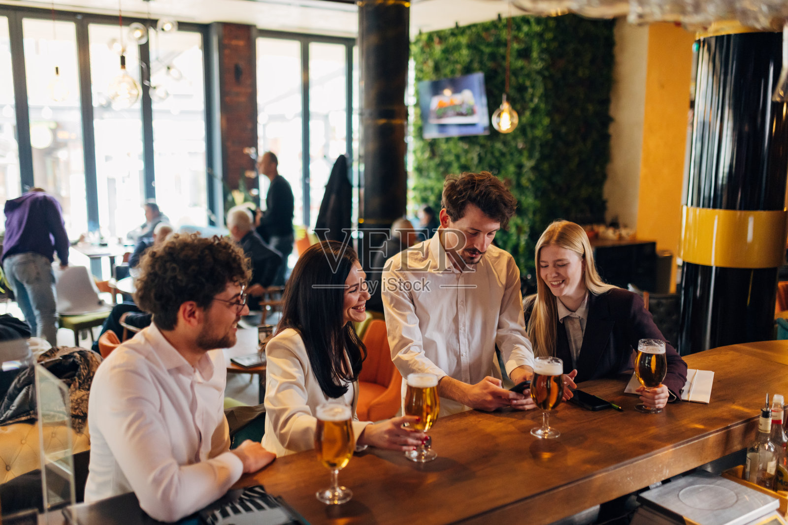 四个面带微笑的商人在酒吧里闲逛，喝着啤酒，用着手机照片摄影图片