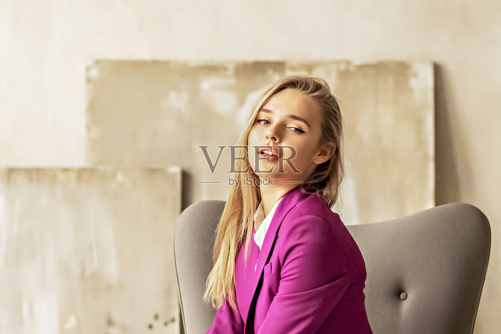 一位留着金色长发的年轻女商人坐在办公椅上。一位漂亮的女董事、经理、总经理、首席执行官，穿着时髦的亮粉色紫红色西装。照片摄影图片