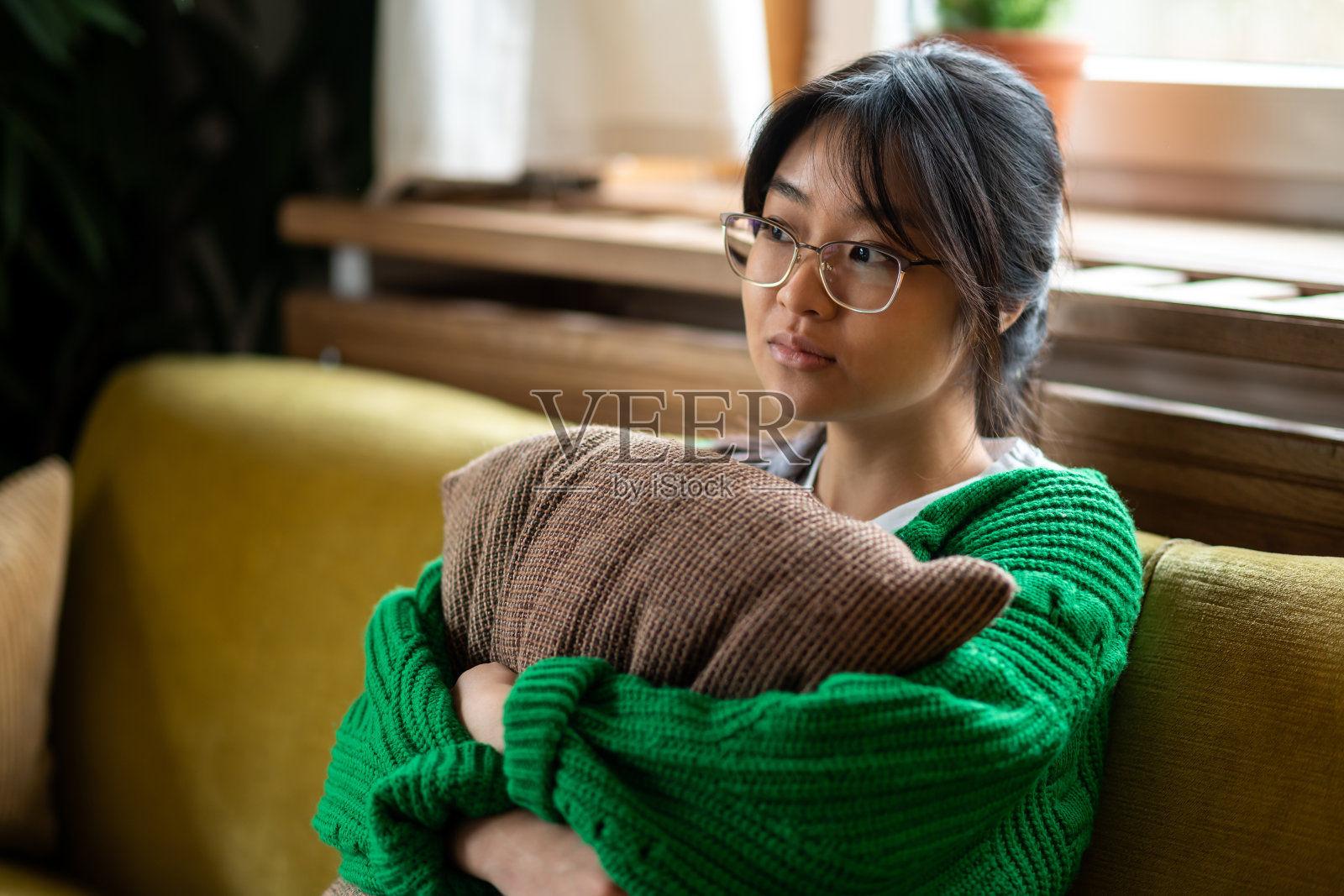 戴眼镜的女孩抱着枕头，看起来很孤独照片摄影图片