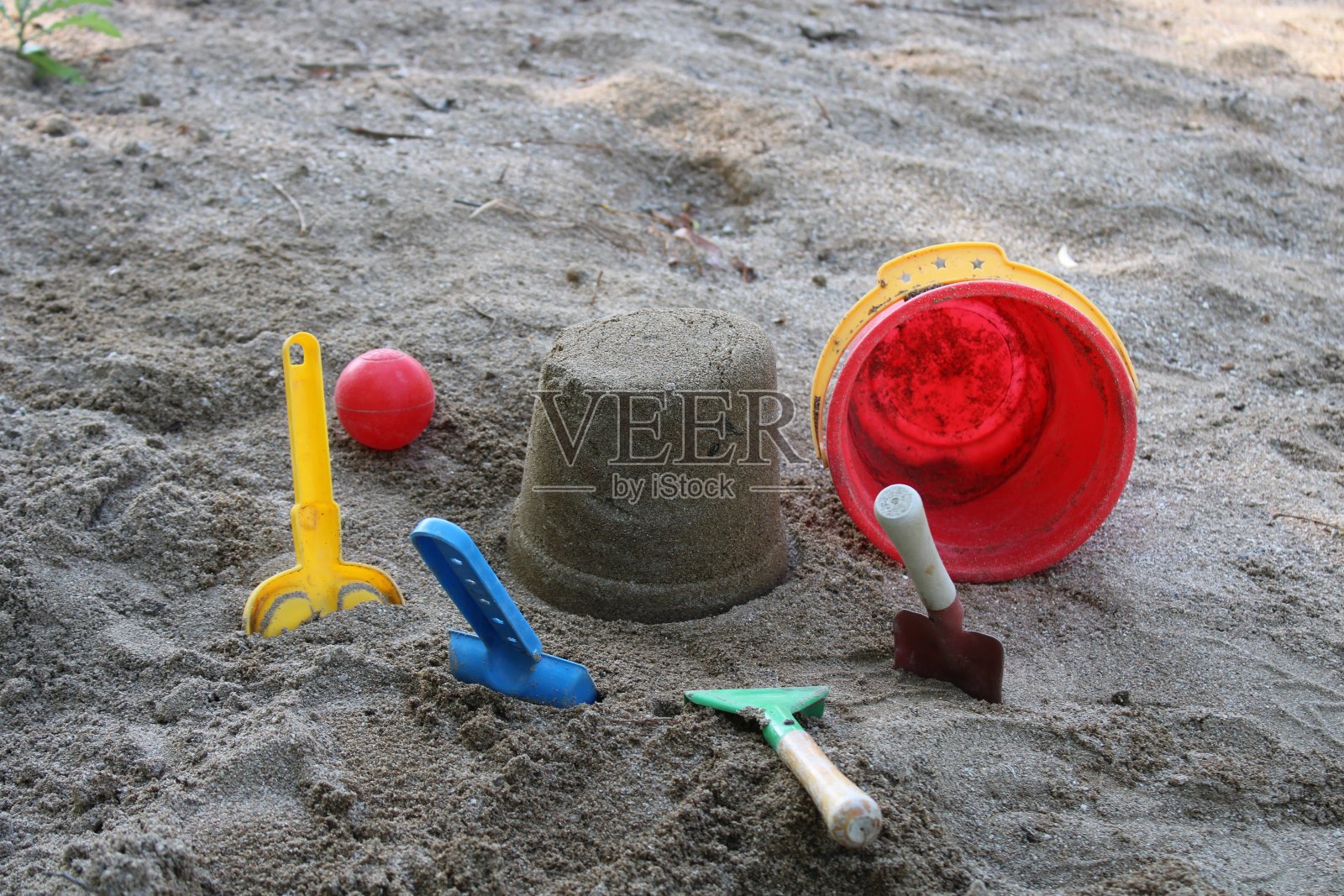 沙子里有一个水桶，旁边是一个红色的球和一个红色的玩具。夏天的时间。海滩上孩子们的玩具照片摄影图片
