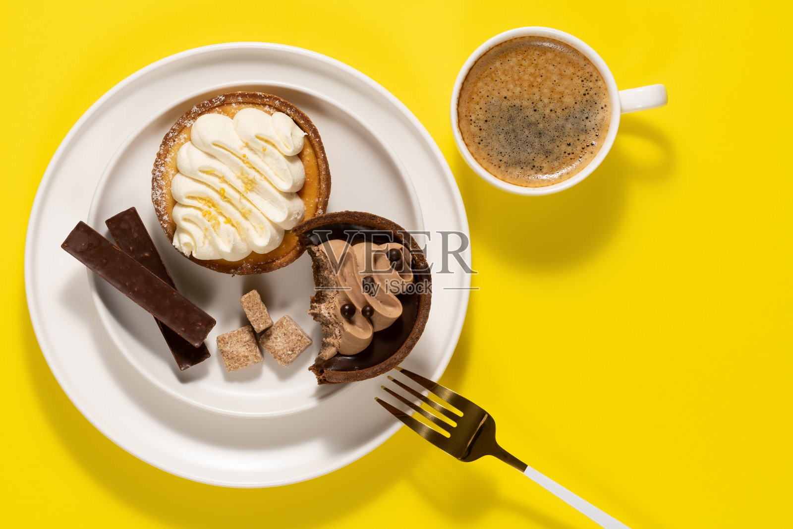 早上的咖啡，美味的蛋糕和盘子里的巧克力。工作时间的午餐。副本的空间。前视图。黄色背景照片摄影图片