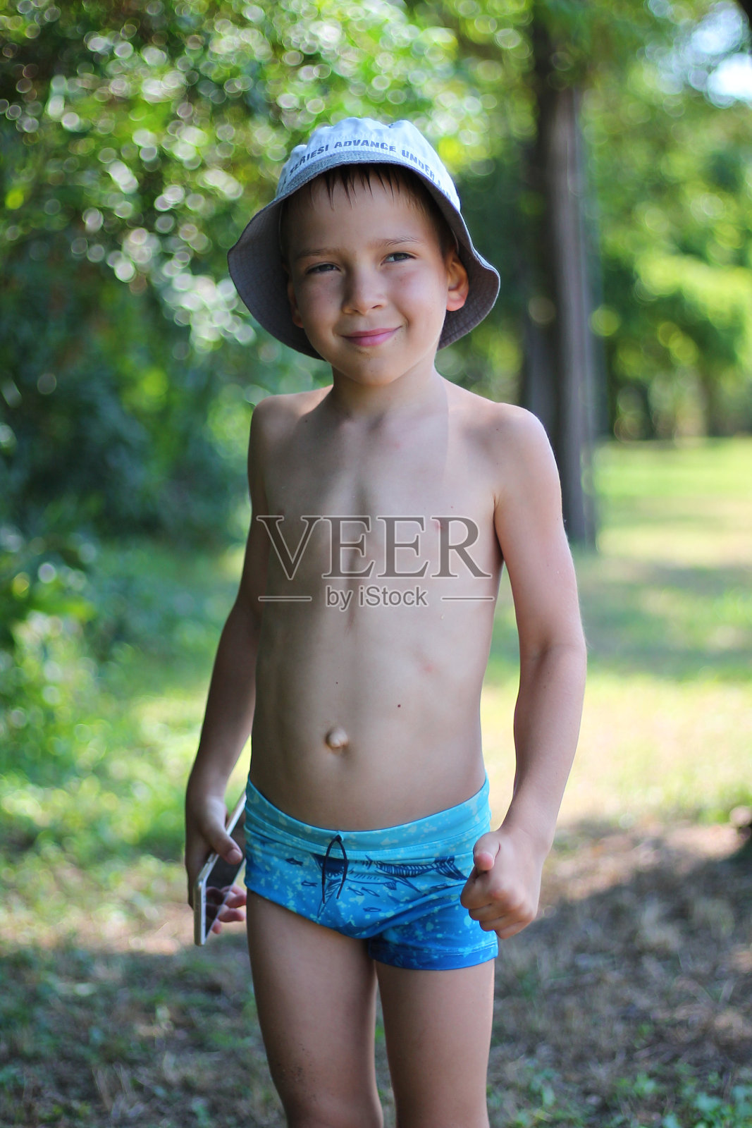 一个穿着泳裤拿着手机的孩子。带着小玩意的夏季海上假期。照片摄影图片