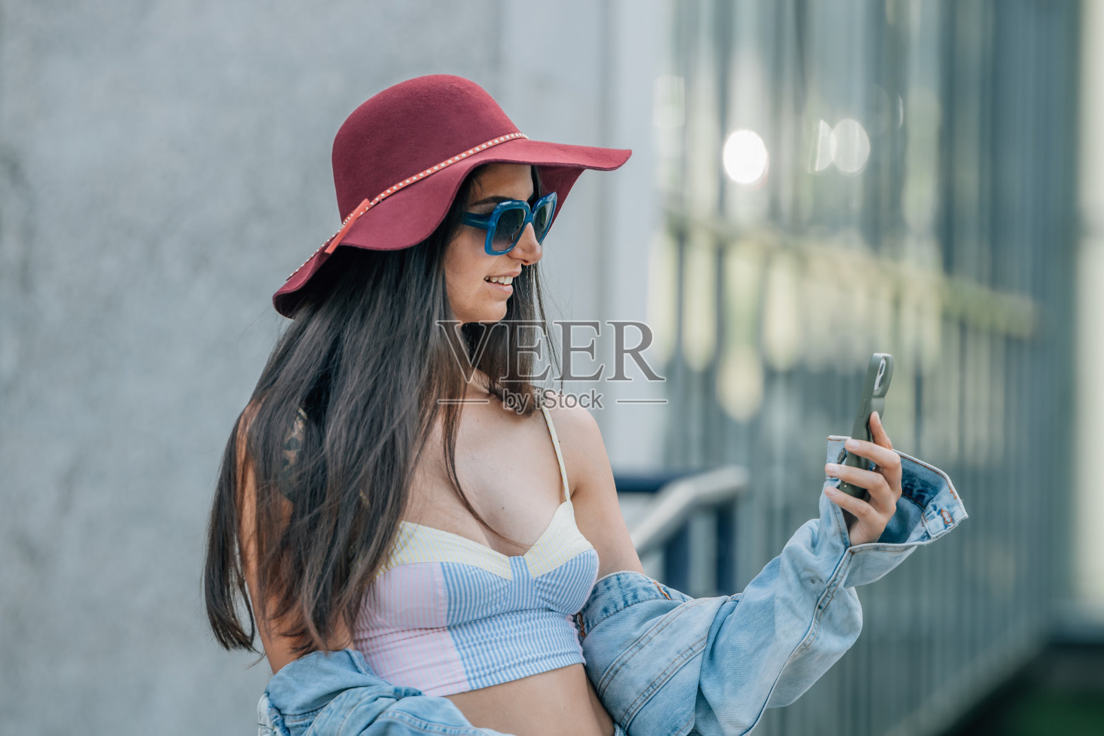 都市时髦女孩戴着帽子和太阳镜，拿着手机或智能手机照片摄影图片