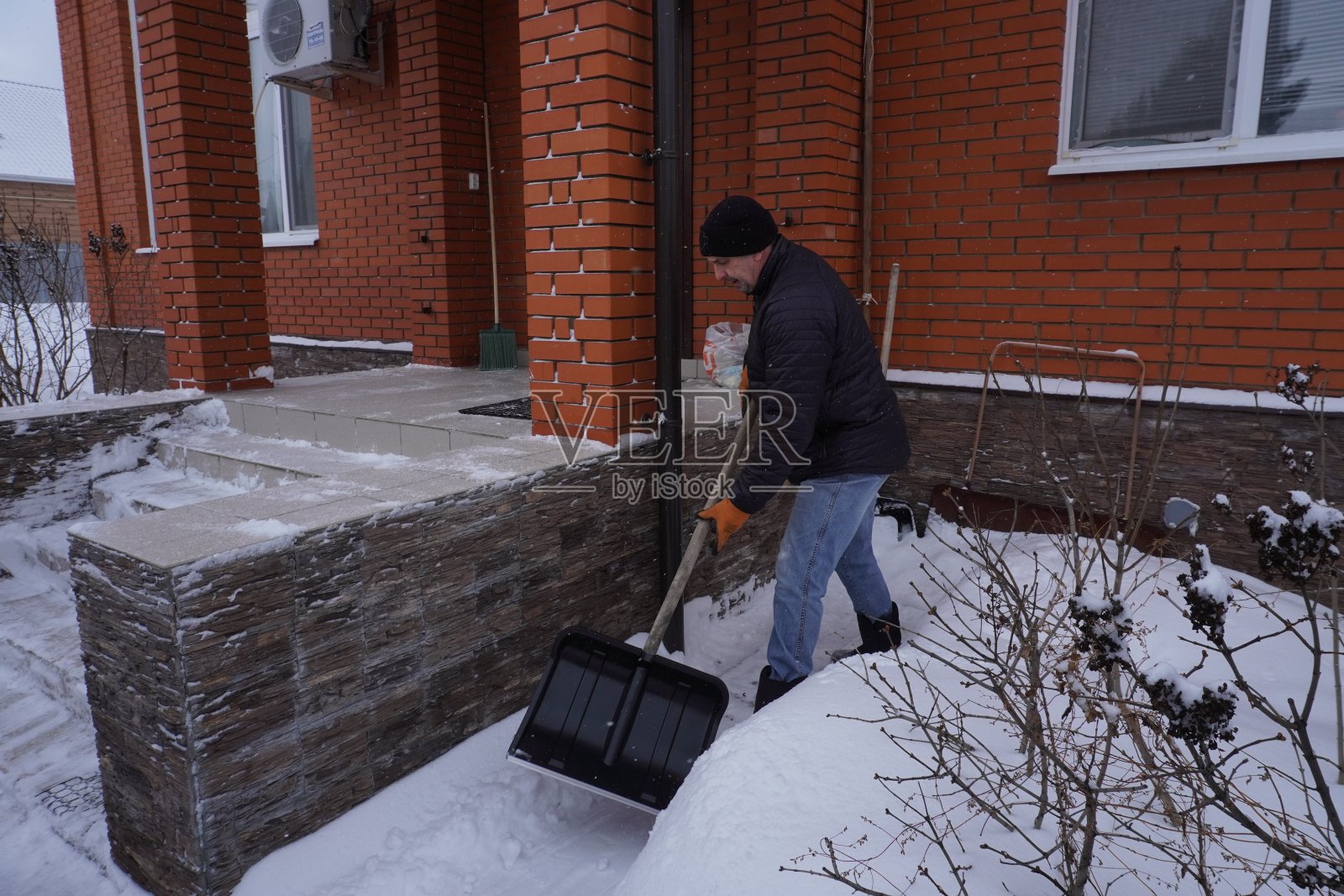 冬天，一名男子在房子的院子里清扫积雪照片摄影图片