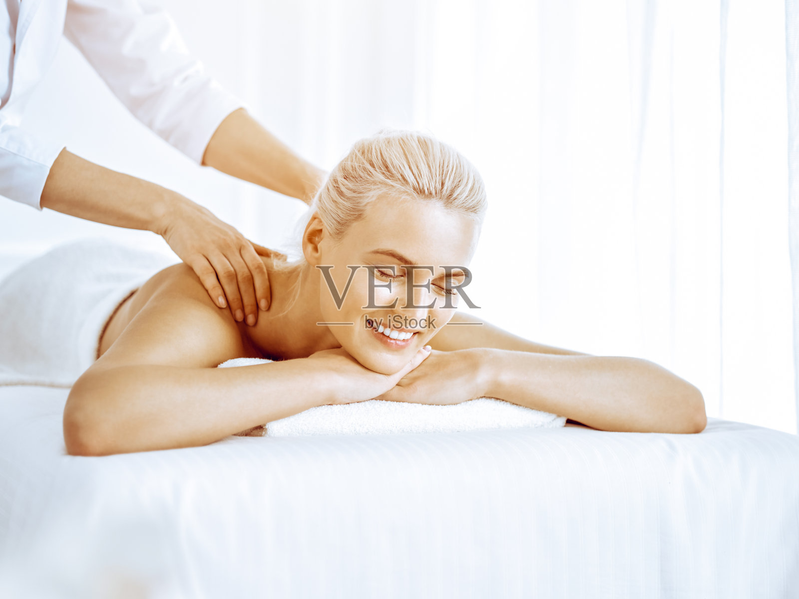 美丽的金发女郎在水疗中心享受背部按摩。美与生活方式照片摄影图片