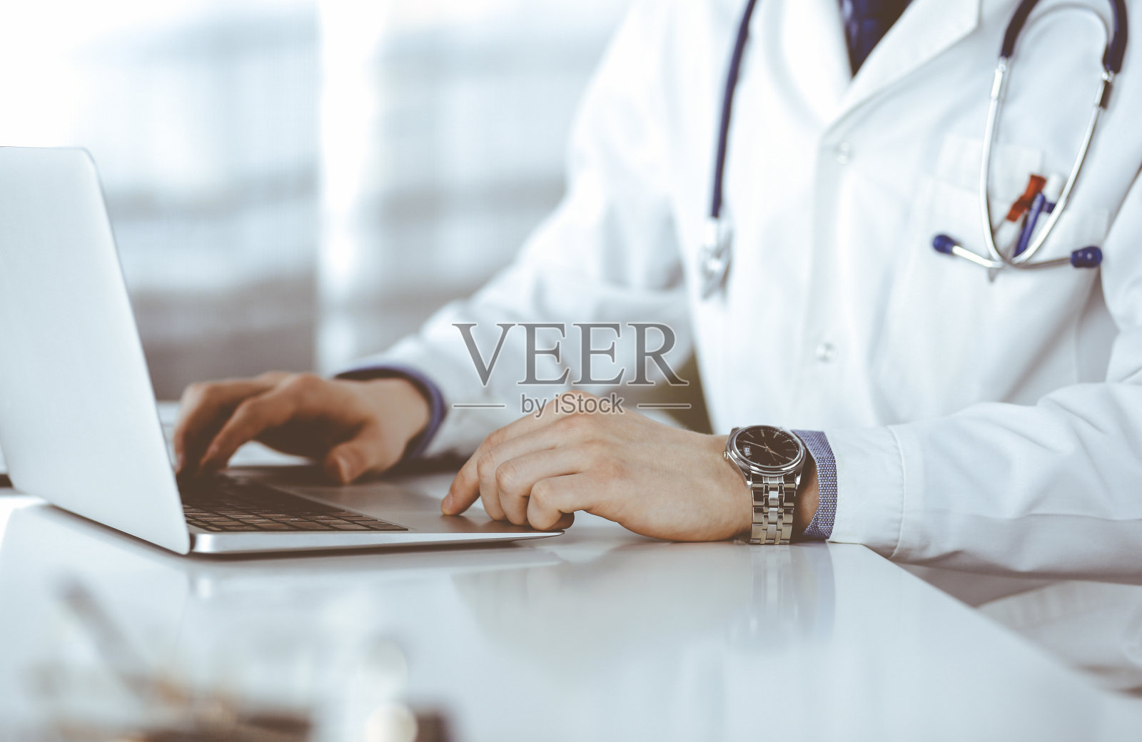 不明身份的男医生坐在诊所里用笔记本电脑工作在他的工作地点，特写。年轻的医生在工作。完善医疗服务，医学理念照片摄影图片